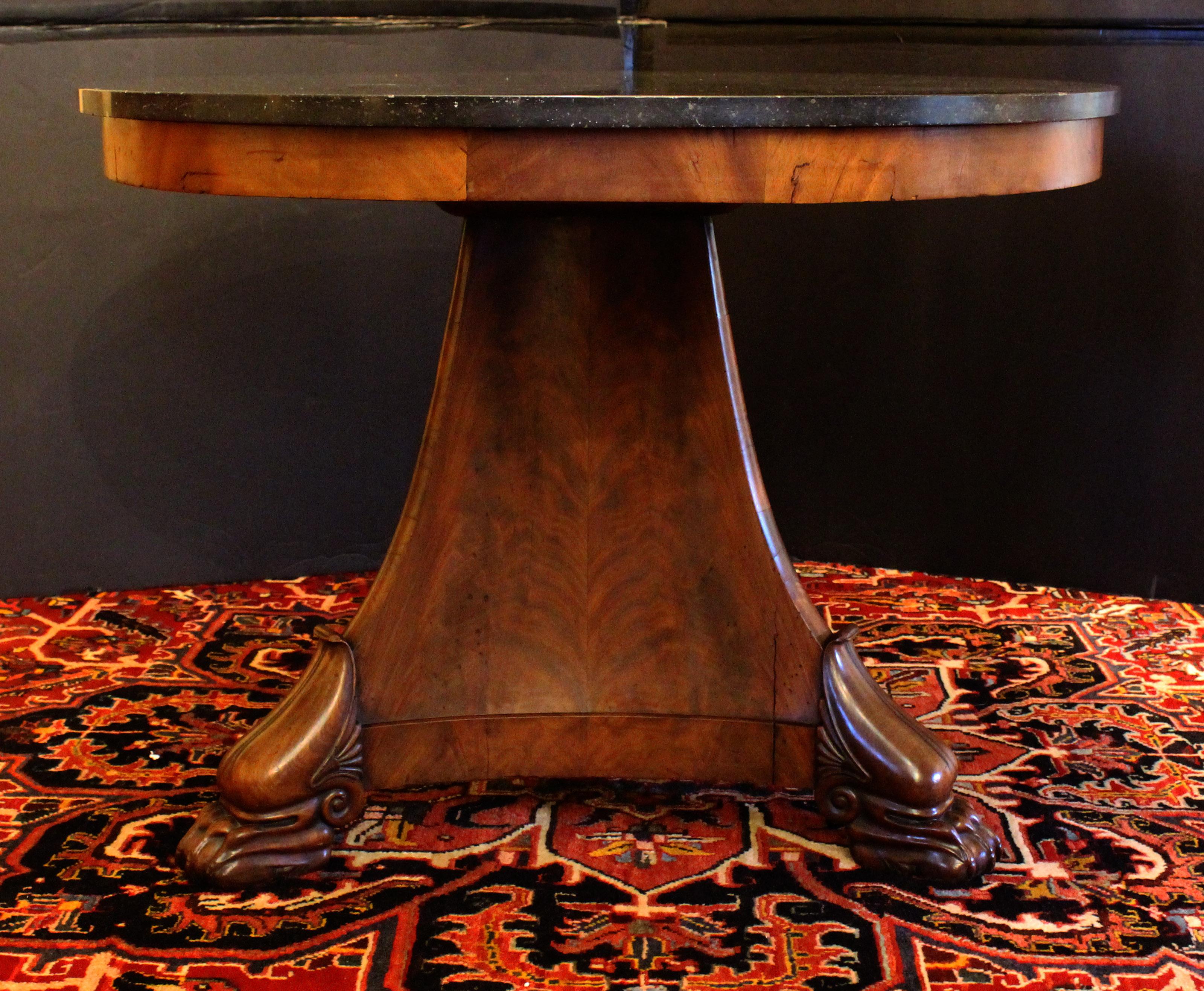 Early 19th century marble top gueridon center table, French. Mahogany, the sides of well figured flame mahogany. Graceful triangular sloped, concave side base ending in three well developed lapet, fan scrolling & paw feet. Old burn mark near base of