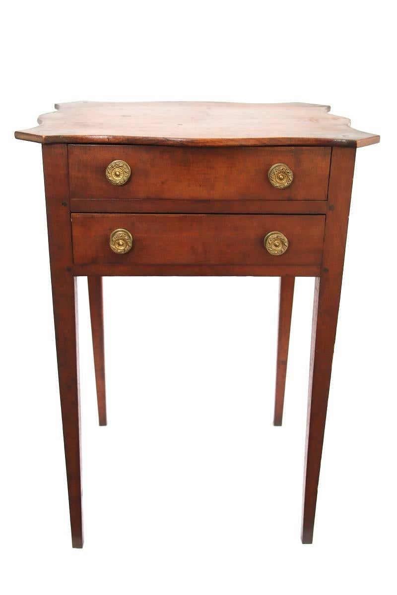Two-drawer work table in cherry features a beautifully scalloped top above two drawers with original brass knobs having square tapering legs

Probably Newburyport, MA, circa 1810.

Provenance: Gary F. Yeaton 

Dimensions: 28” H X 16” D X 19 ¾”