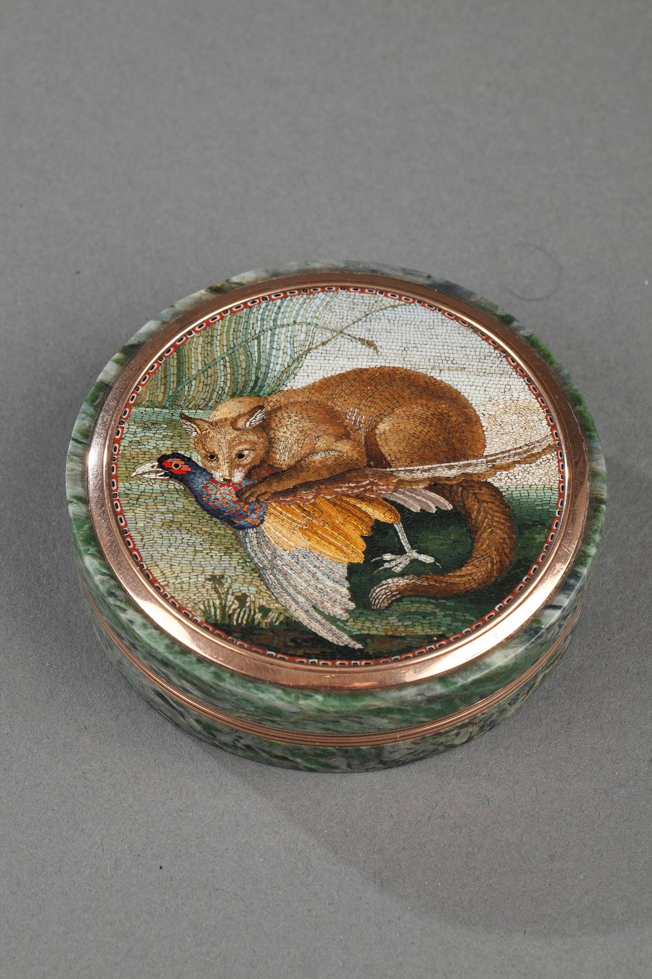 Round box made in hardstone (green porphyry). The removable lid is decorated with a circular micromosaic of exceptional quality. It features a fox attacking a pheasant. The fox near a clump of reeds, is crouched, ears back, and remains wary of his