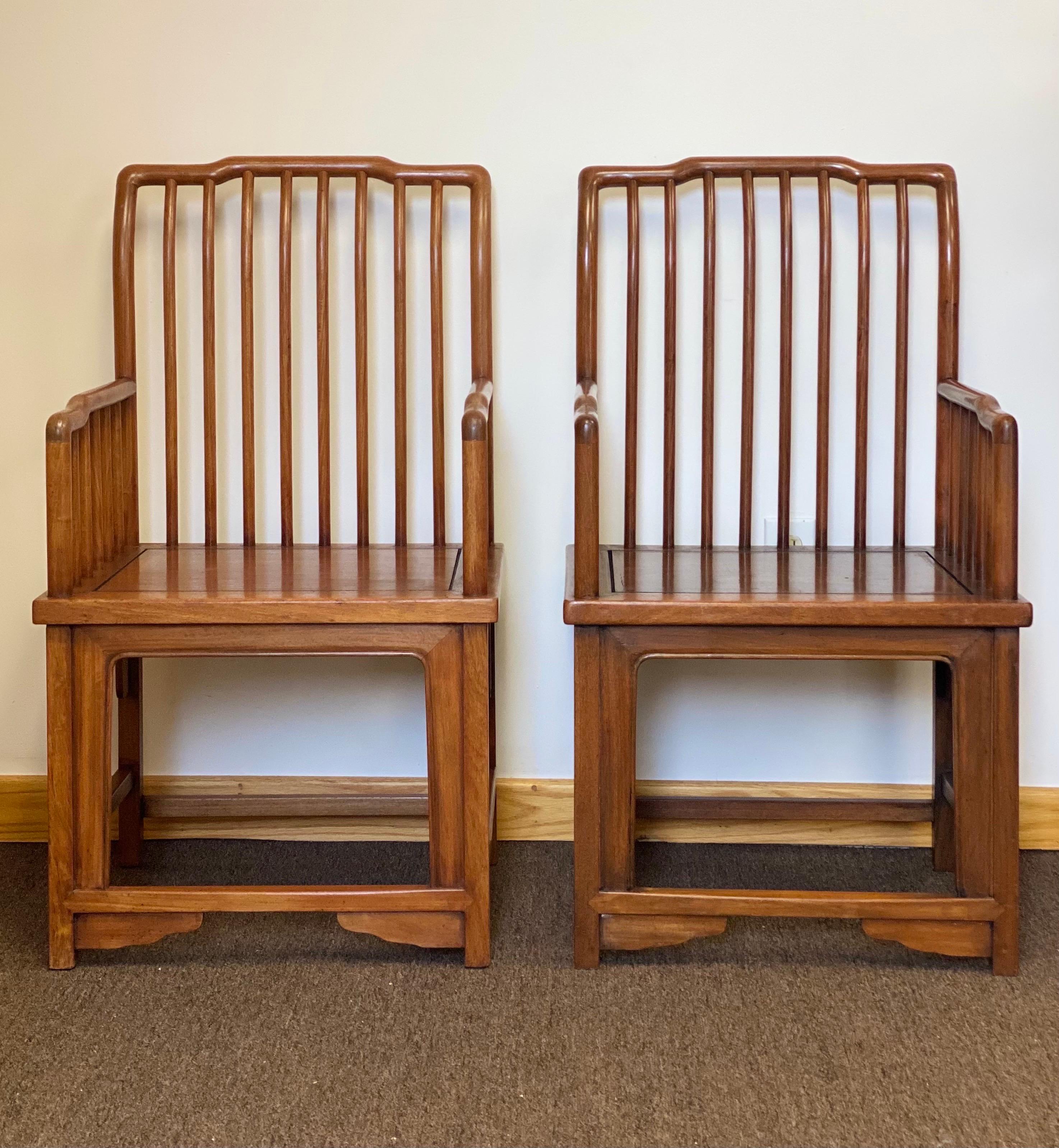 We are very pleased to offer a pair of beautiful Chinese Ming Style armchairs, circa the early 19th century. This structural, clean-lined pair is handcrafted of solid hardwood with a slatted back and armrests. The front opening underneath the seat