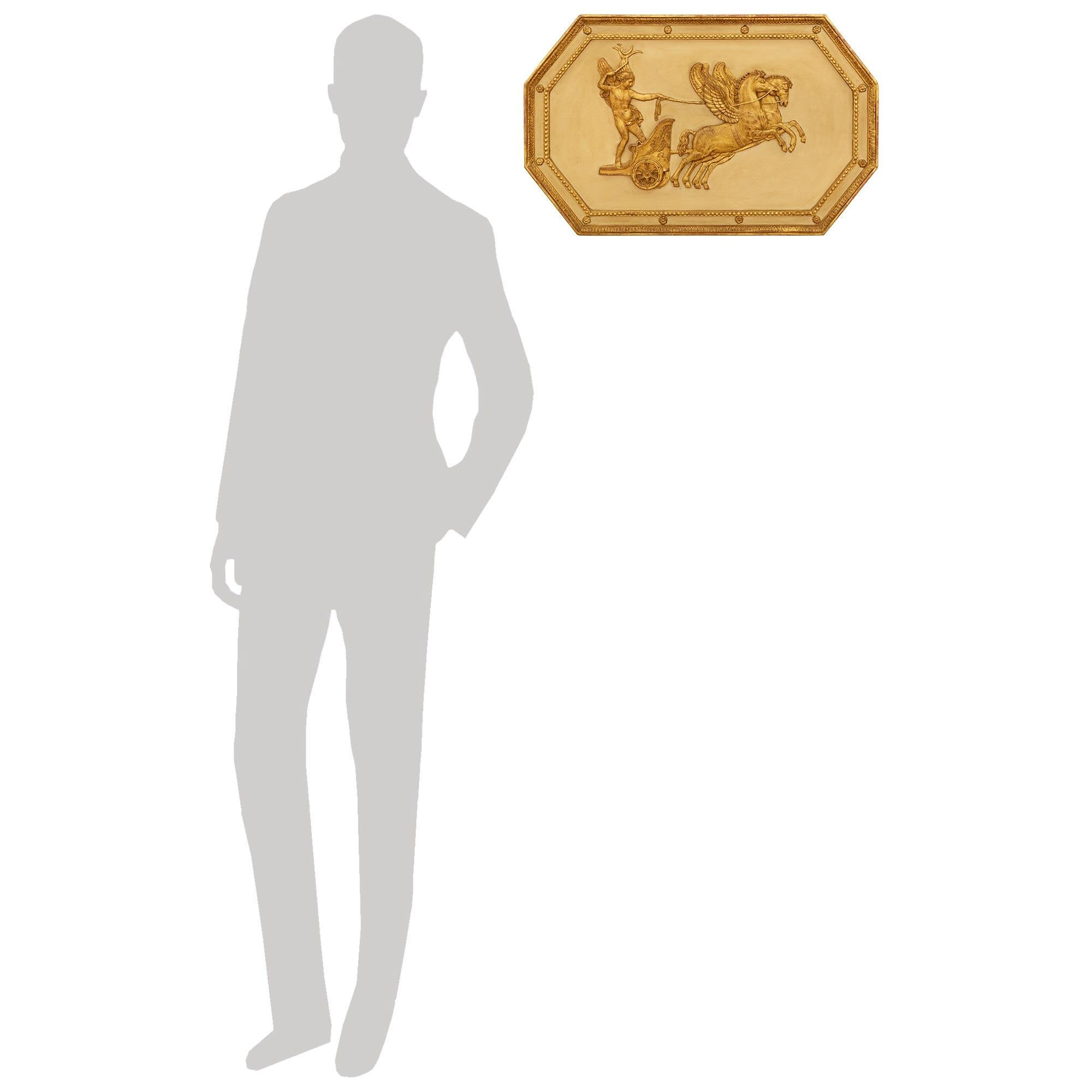 Plaque en bois et bois doré patiné de style néo-classique italien du début du 19e siècle, attrayante et très décorative. Ce magnifique panneau de décoration murale de forme octogonale représente Eros, également connu sous le nom de Cupidon, avec ses