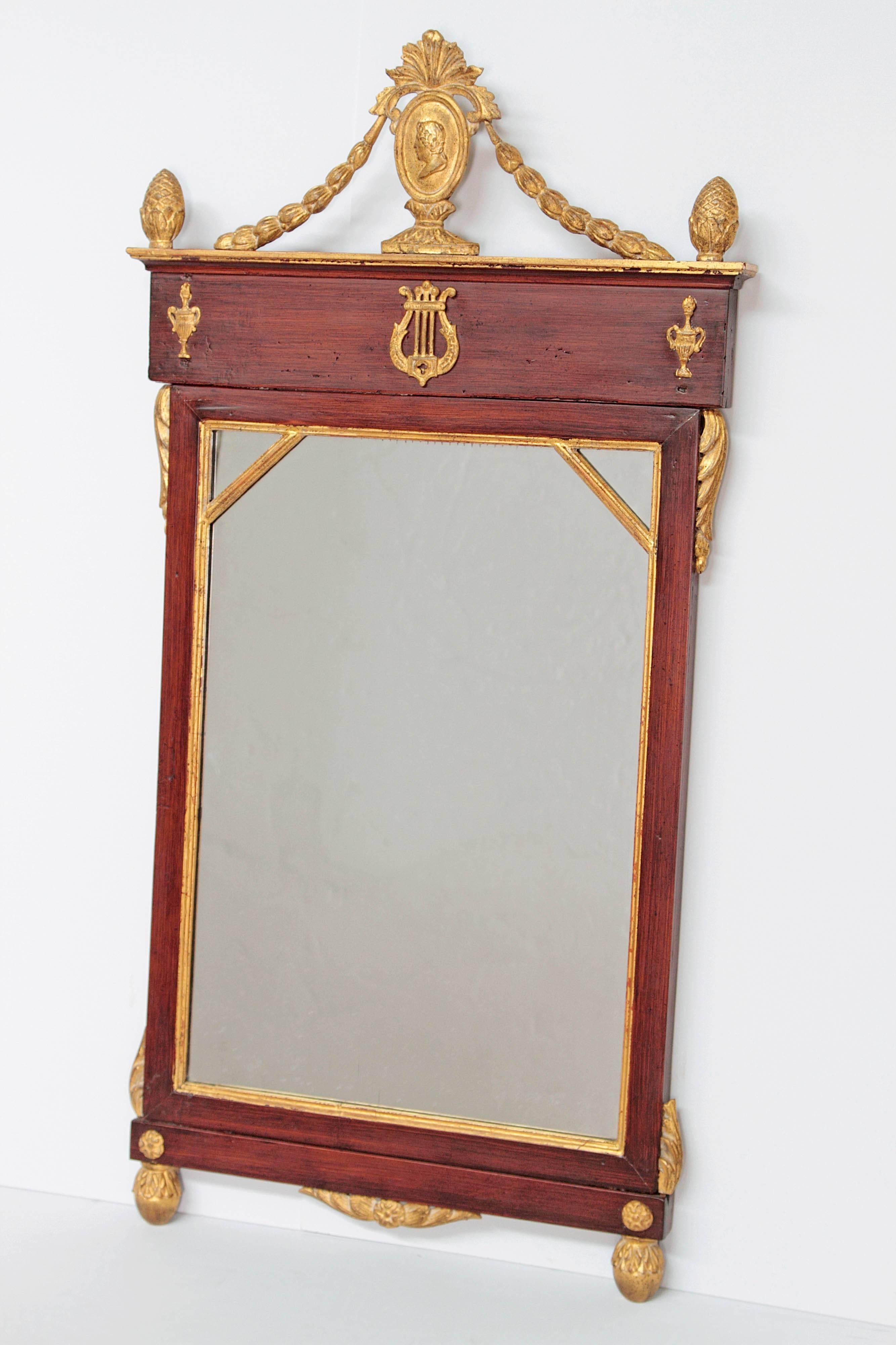 A mahogany and giltwood neoclassic mirror. Portrait of Classic figure in oval at top with swags to frame. Applied urns as sides and lyre in center, all gilt as well as around mirror. Additional decorations on sides and as the corners. Early 19th