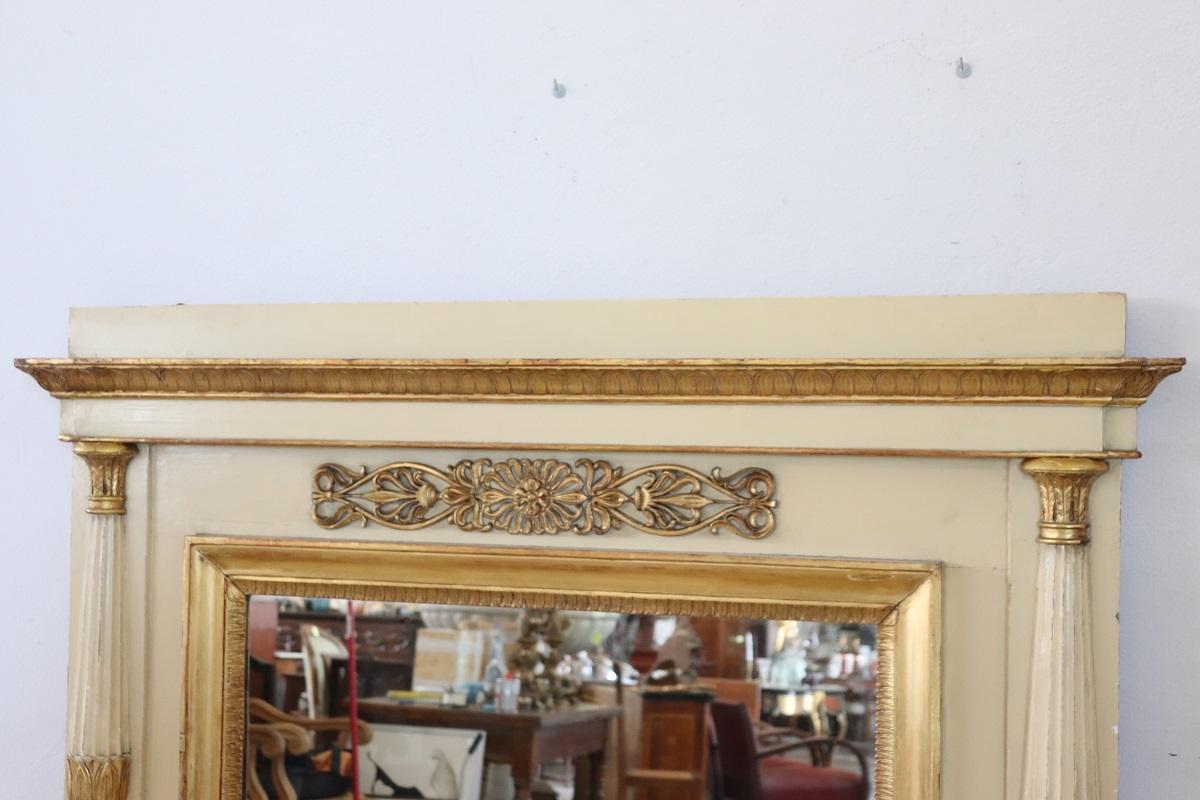 Este elegante espejo de pared neoclásico antiguo es una pieza llamativa, que refleja tanto el encanto histórico como la belleza atemporal. Fabricado en madera finamente tallada, el espejo luce intrincadas decoraciones neoclásicas en pan de oro que