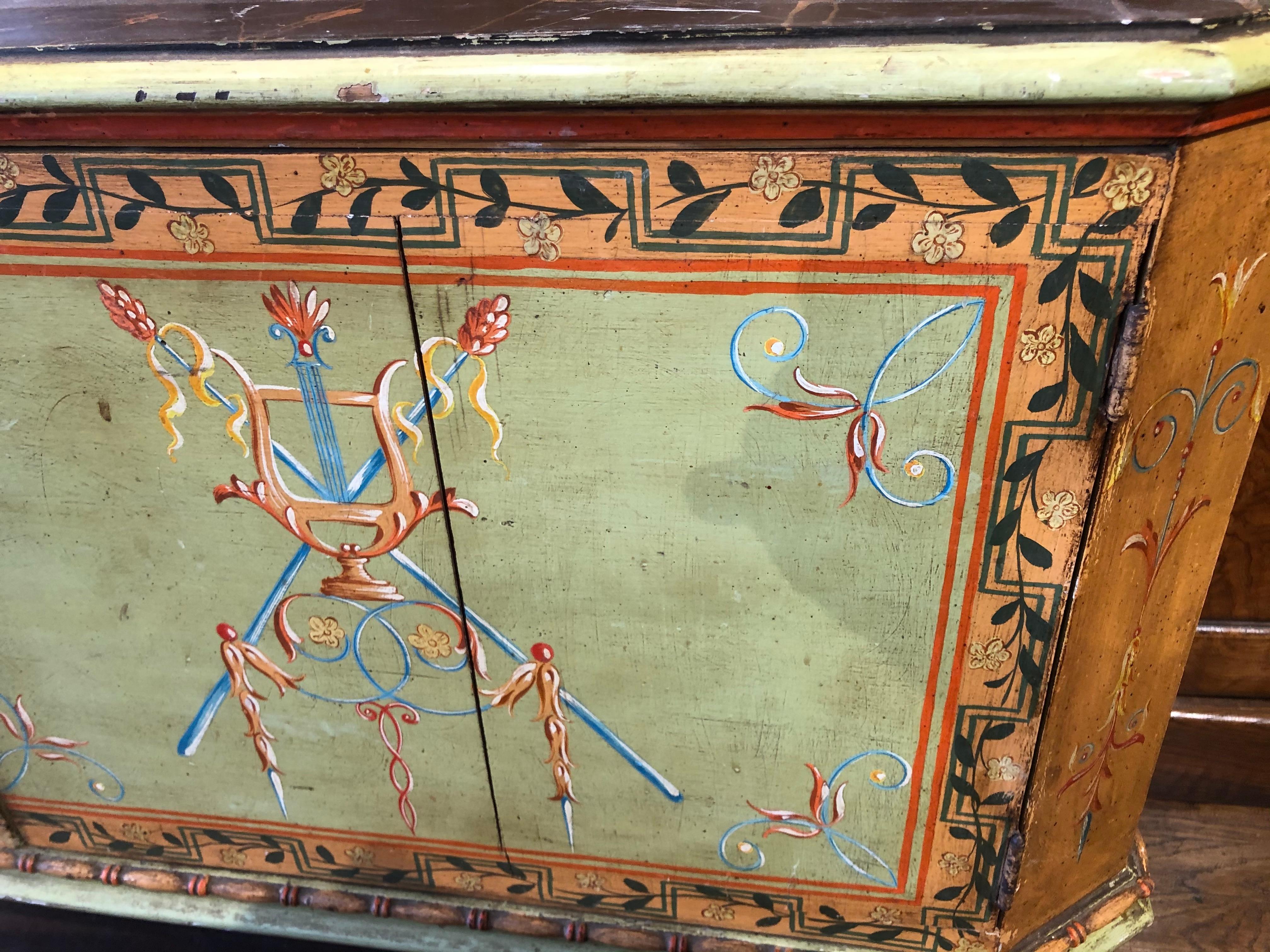 A beautifully preserved example of early 19th-century Italian craftsmanship, this neoclassical painted cabinet was made in Tuscany circa 1820. The piece retains its original hand-painted polychrome decoration in soft green, terracotta, and black