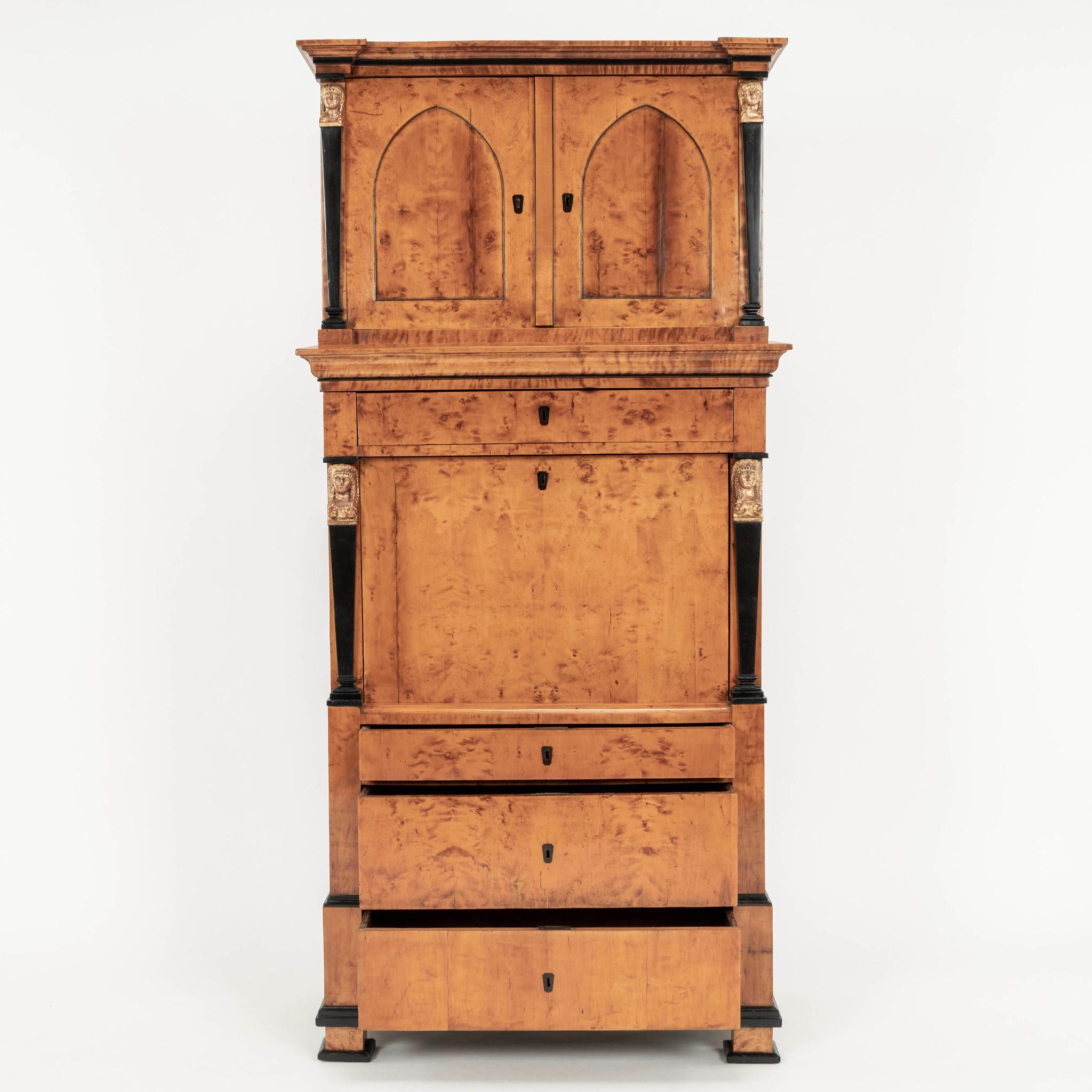 An extraordinary early 19th Century Neoclassical style Karelian birch secretary. This wonderful cabinet features four ebonized columns supporting giltwood caryatids, two gothic arched cabinet doors, a myriad of  compartments, shelves, drawers