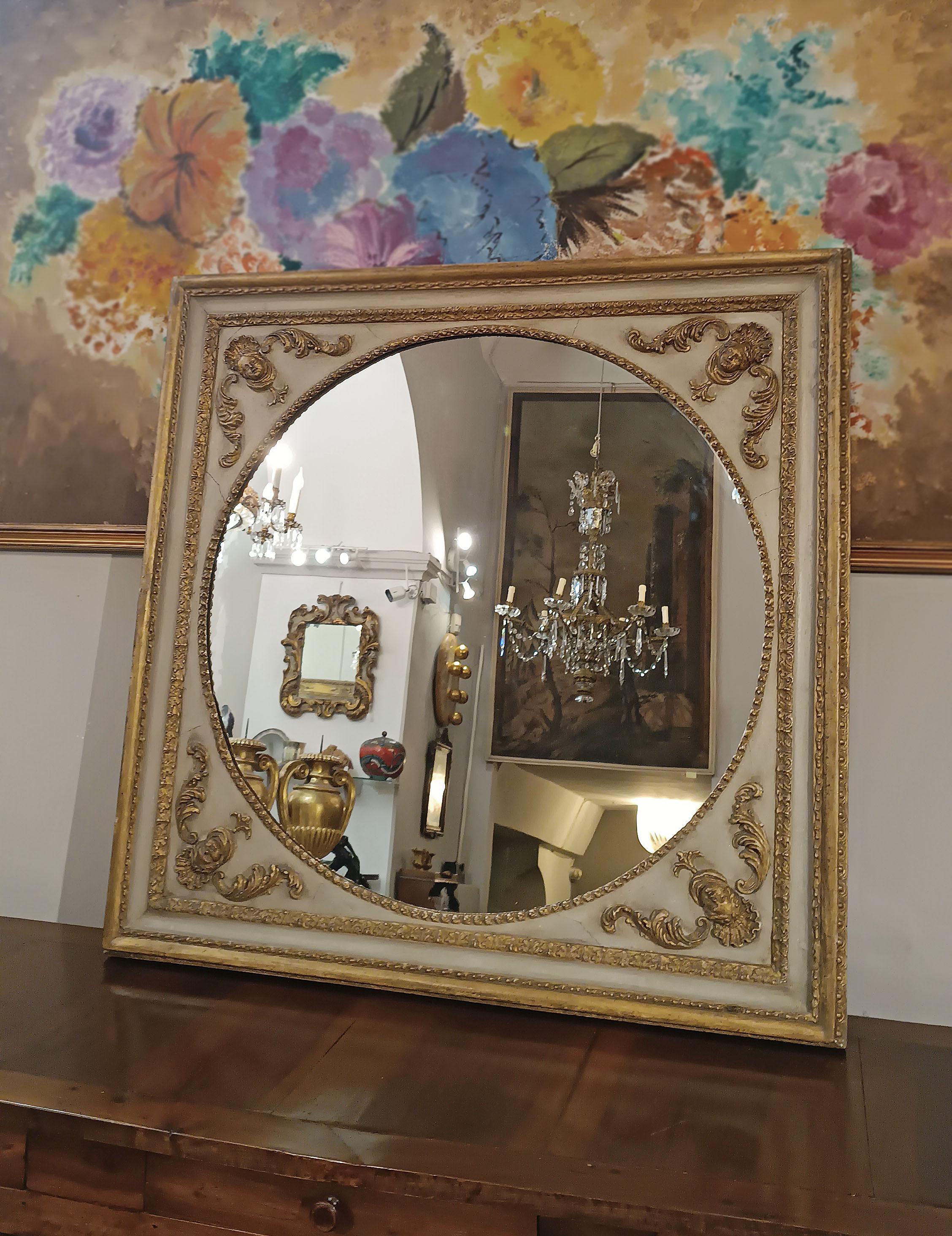 Elegant mirror with a square frame in carved wood, partially painted and gilded, enriched with pastille. The mirror, of circular shape, gives a further touch of refinement. The frame is adorned with decorations of vegetal garlands, while on the
