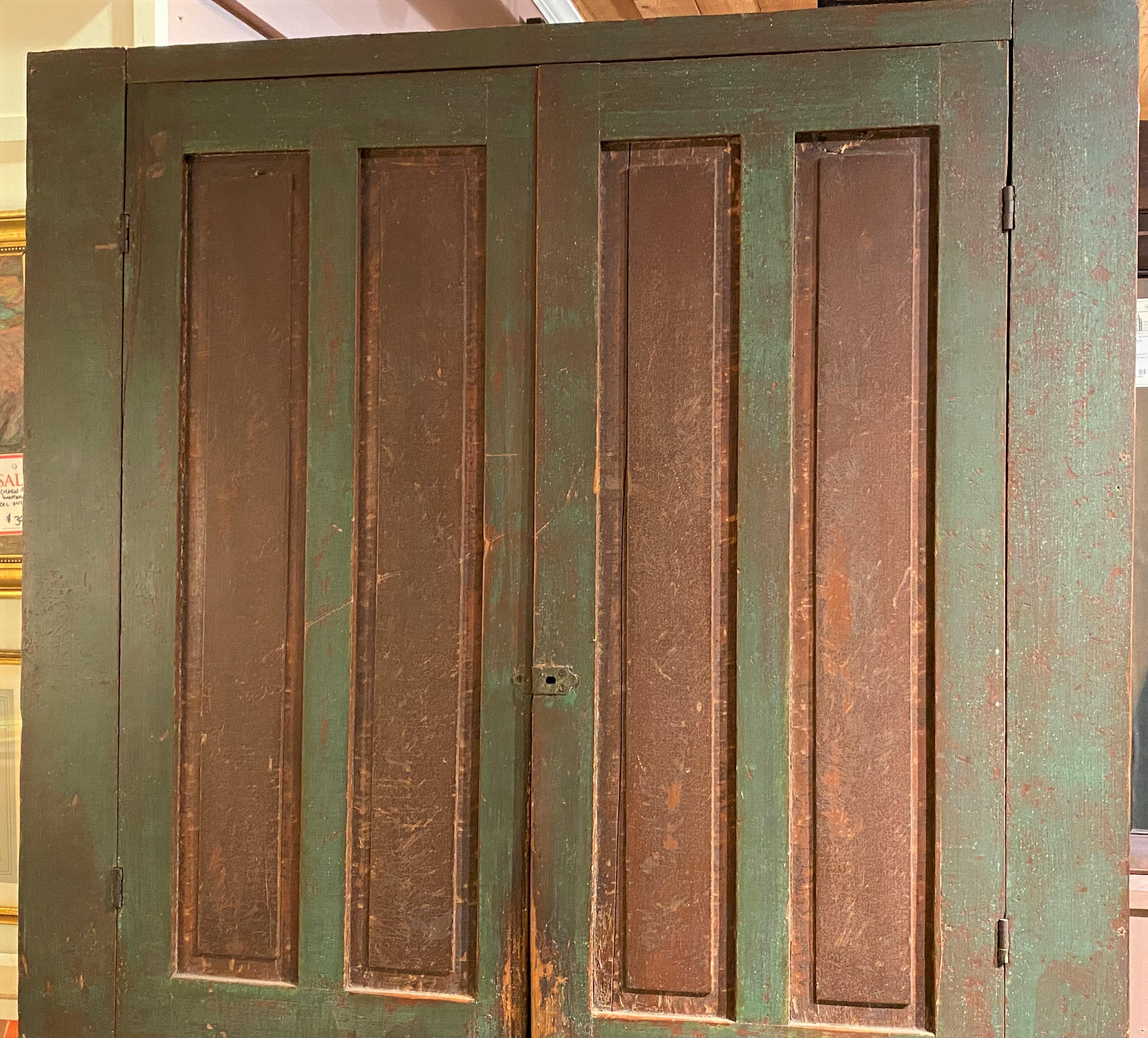A wonderful large New England pine four door cupboard with double panels on each door, opening to four interior shelves, in old green paint with reddish brown panel highlights and nicely carved skirt at the base. The cupboard dates to the early 19th
