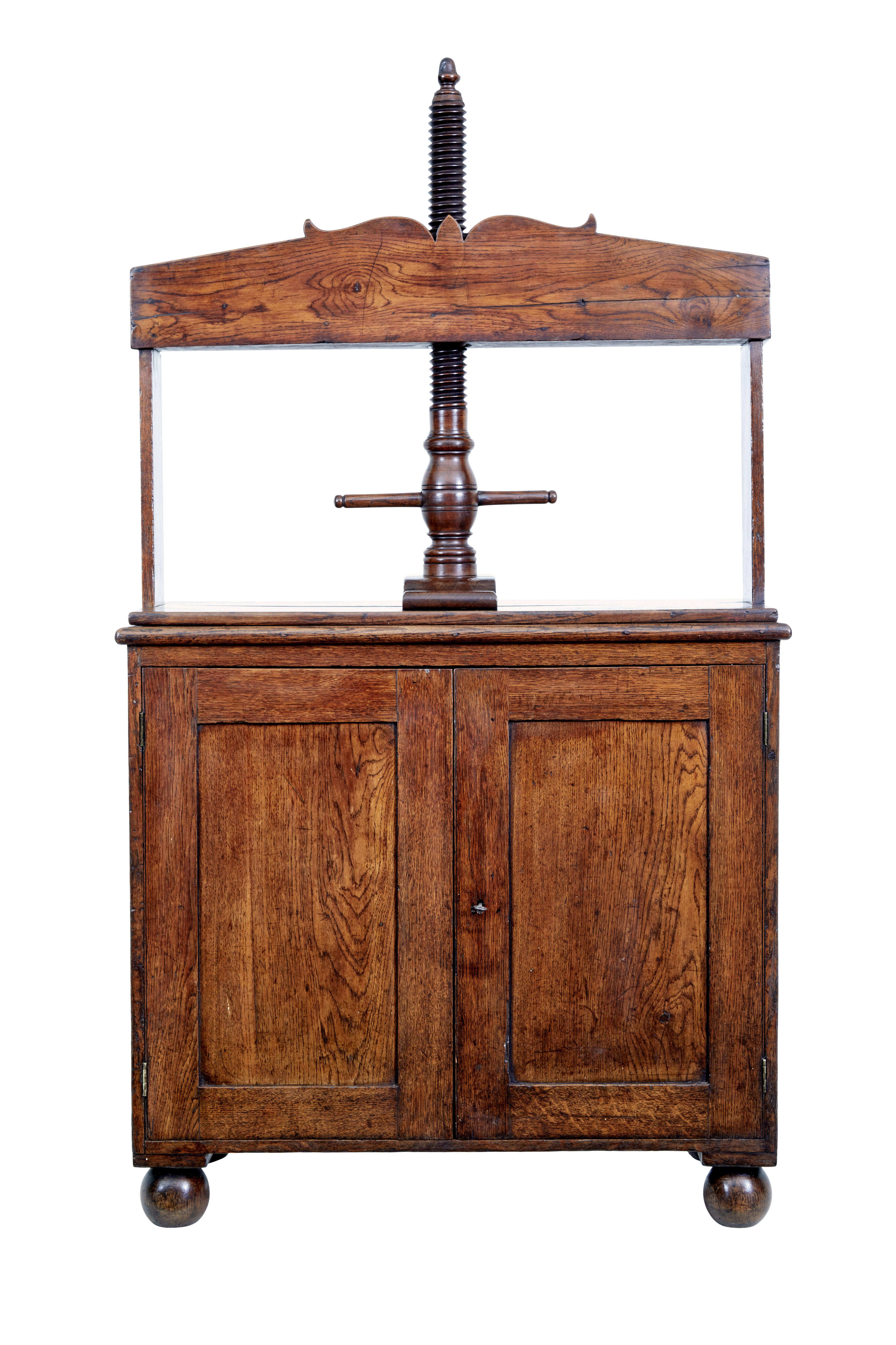 Early 19th century oak book press cupboard circa 1800.

One piece georgian book press made from solid oak.  Hand carved spiral thread which still functions well, turned by a turned arm.  Below which a double door cupboard with working lock and key,