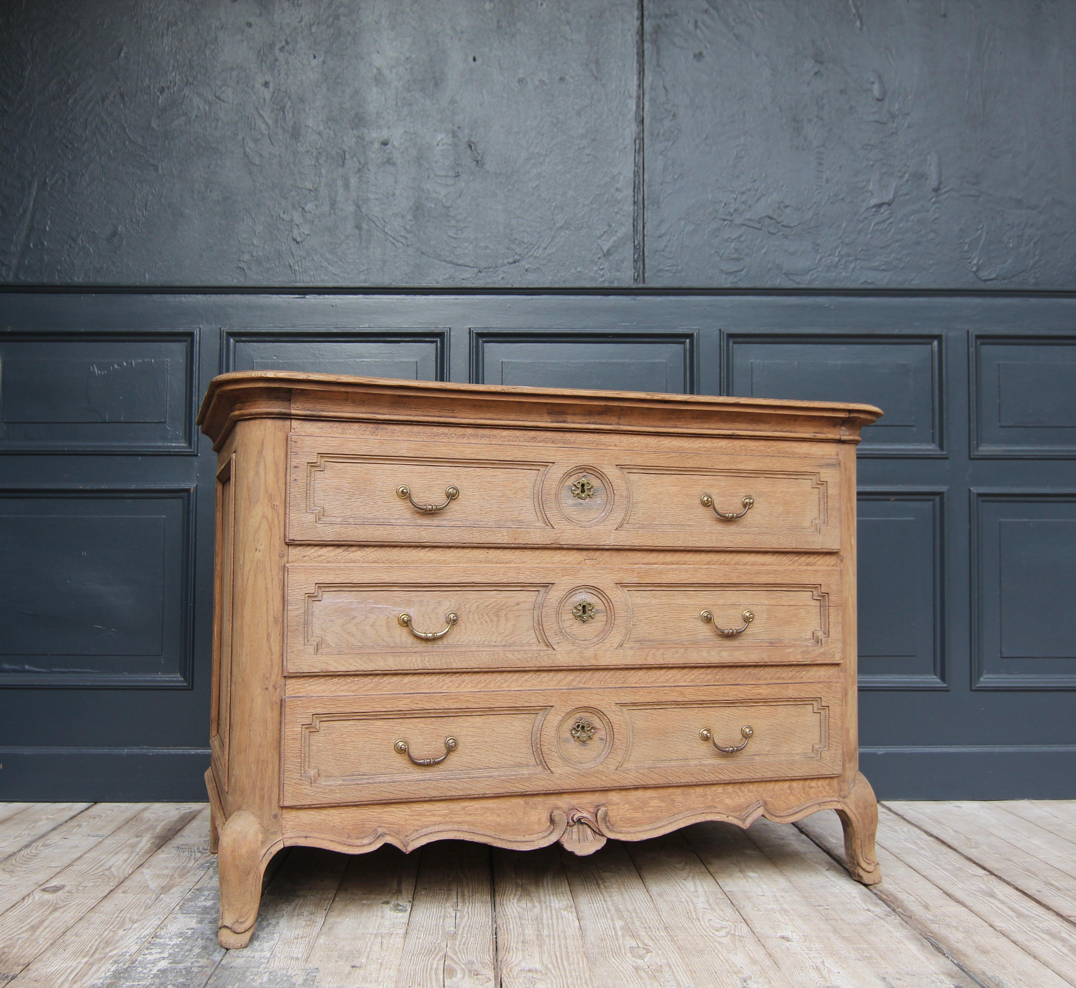 A early 19th century provincial chest of drawers made from solid oak. 

Laterally coffered oak body with three drawers, rounded corners and matching moulded top panel. Multiple curved moulded plinth frame with carved shell-shaped central cartouche