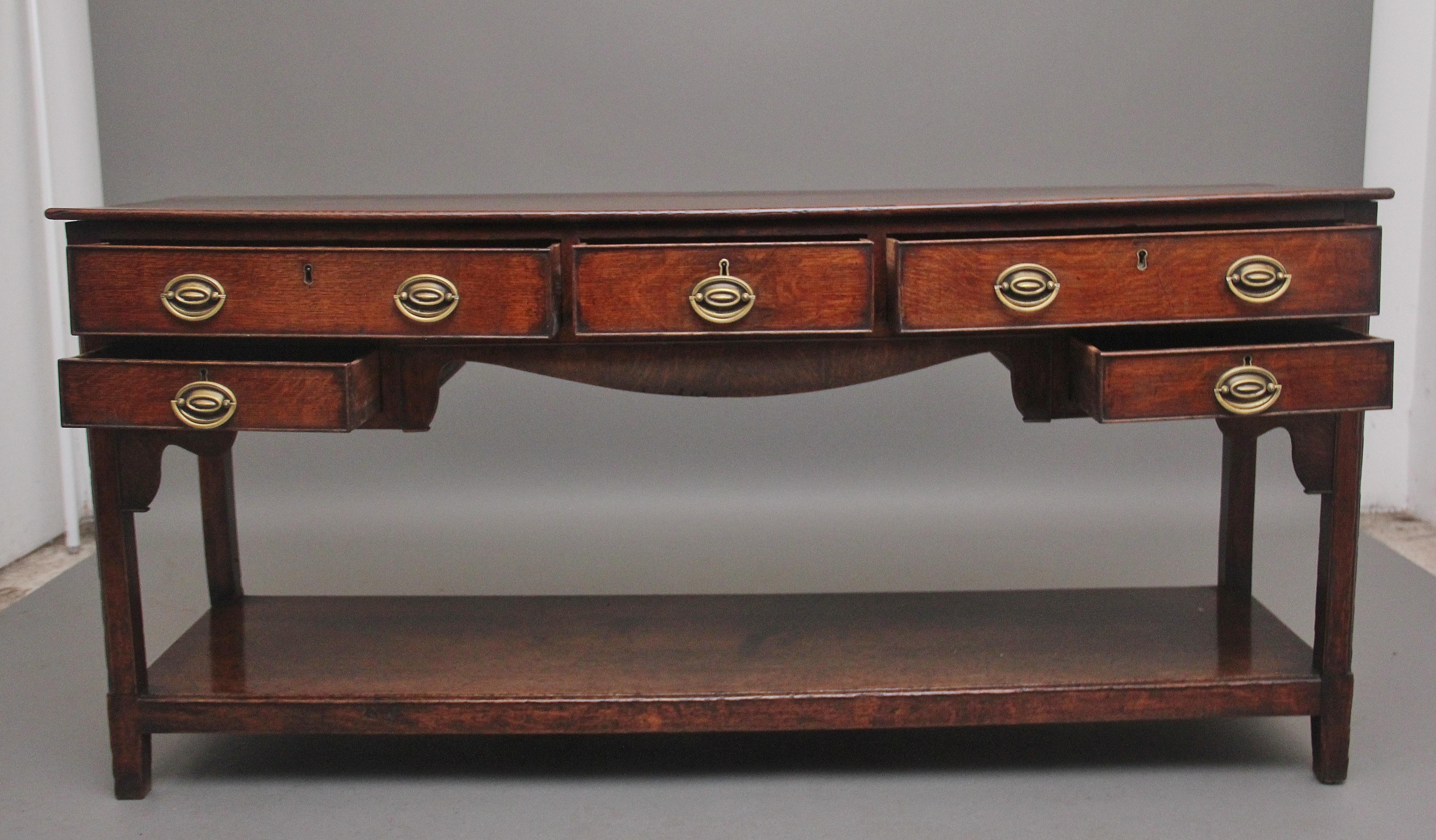 Early 19th Century oak dresser base, having a nice figured rectangular top above a combination of five drawers of different sizes fitted with brass oval plate handles, shaped apron at the centre and shaped corner brackets either side, supported on