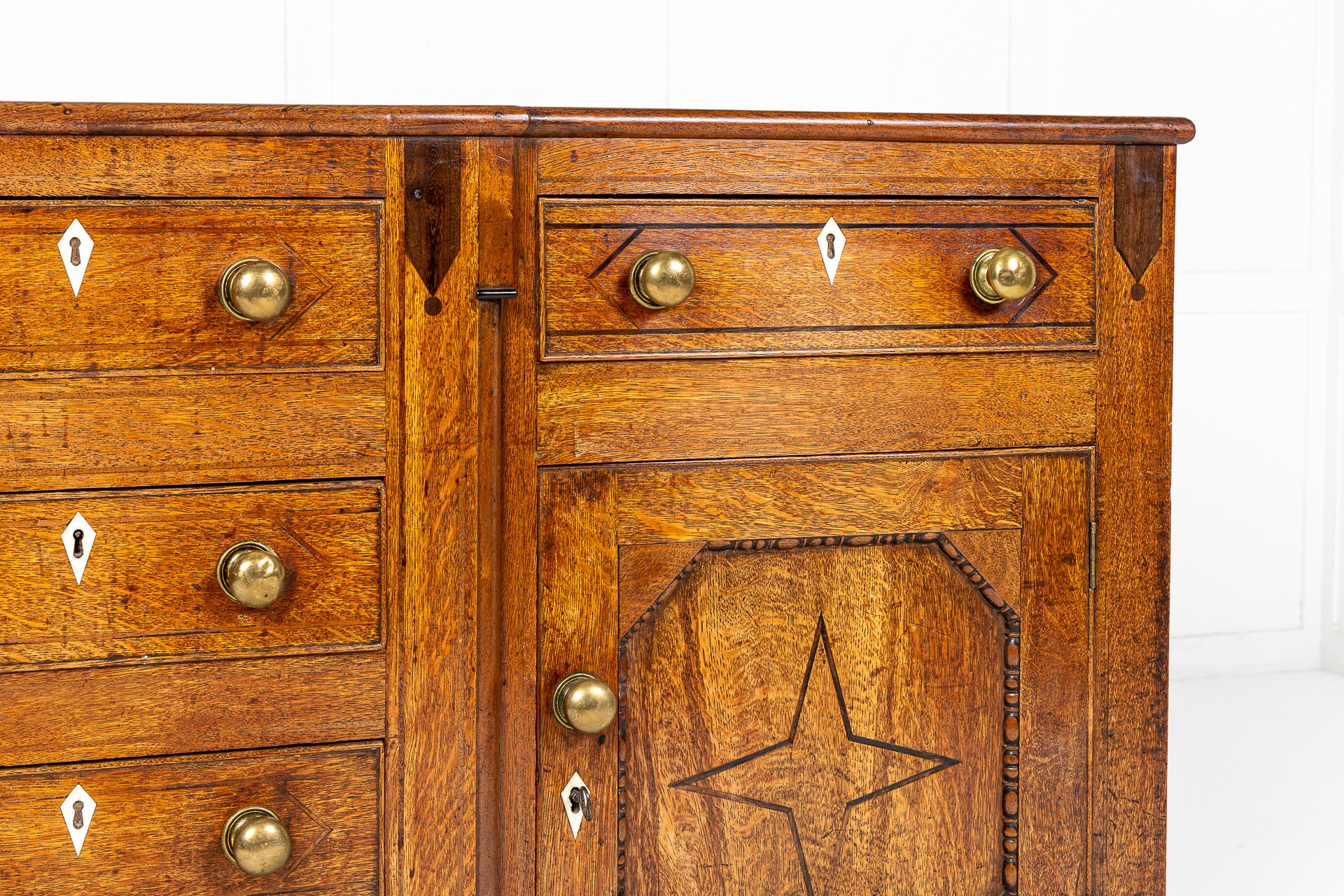 Early 19th century English oak dresser base, having a moulded breakfront top above a central bank of four drawers with brass handles, flanked by cupboard doors either side with lovely, fielded panels having unusual mouldings and mahogany inlaid star