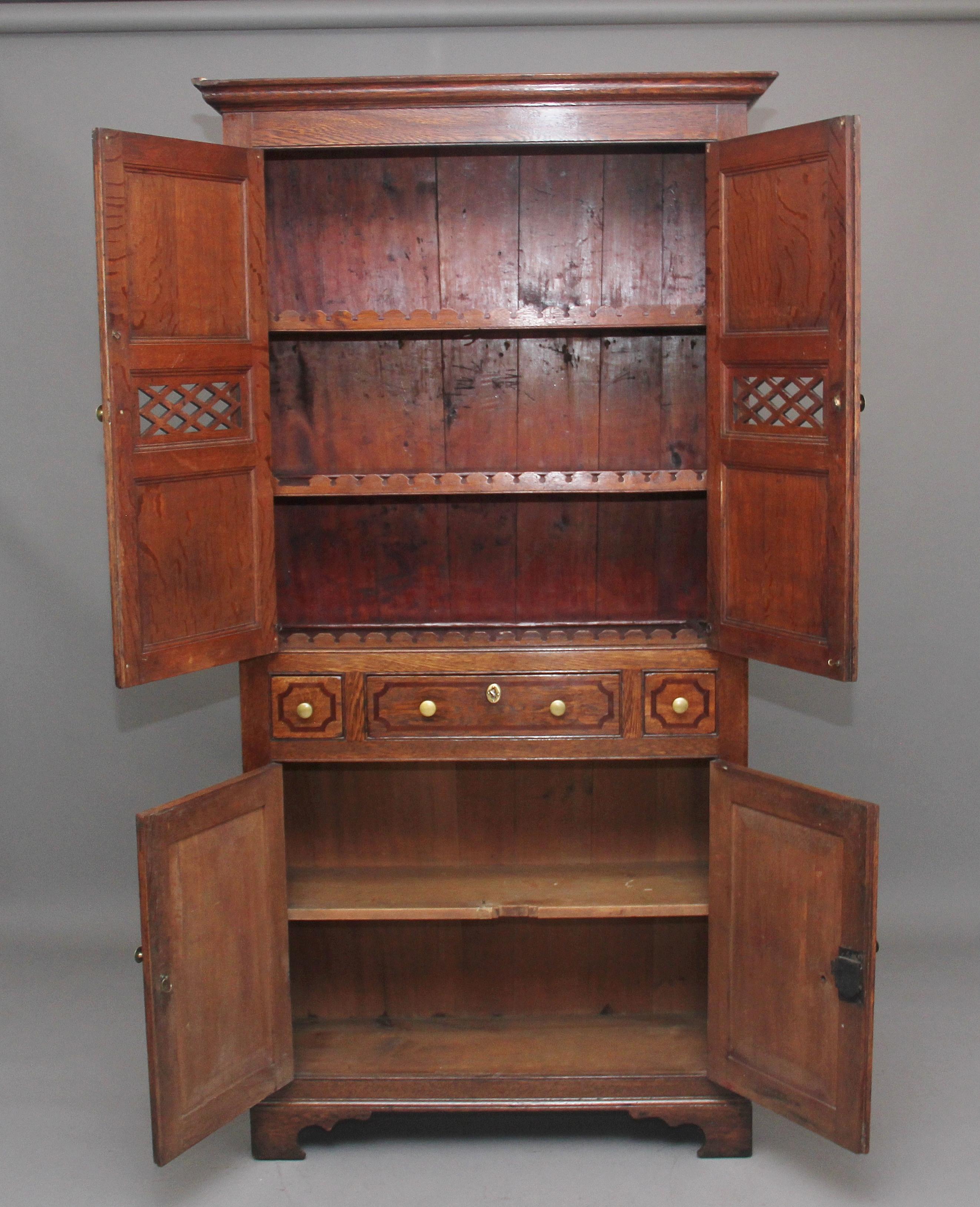 Early 19th century oak food cupboard, having a moulded cornice above quarter sawn oak doors with fielded panels and pierced fretwork sections, opening to reveal shelves with unusual carved mouldings, three drawers below with crossbanded detailing