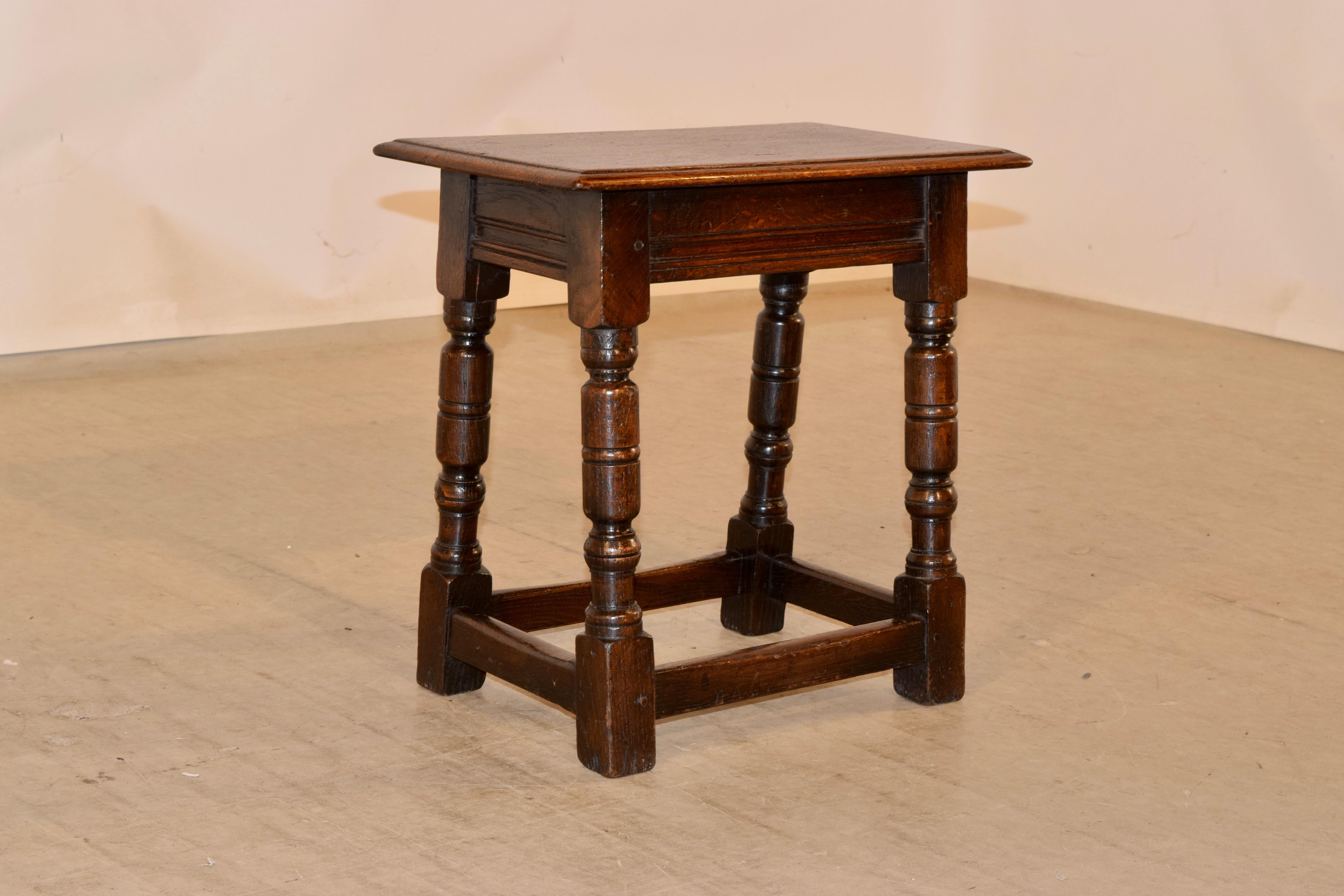 Early 19th century oak joint stool from England with a beveled edge around the top, following down to a simple apron with molded banding. The stool is supported on hand turned splayed legs, joined by simple stretchers.