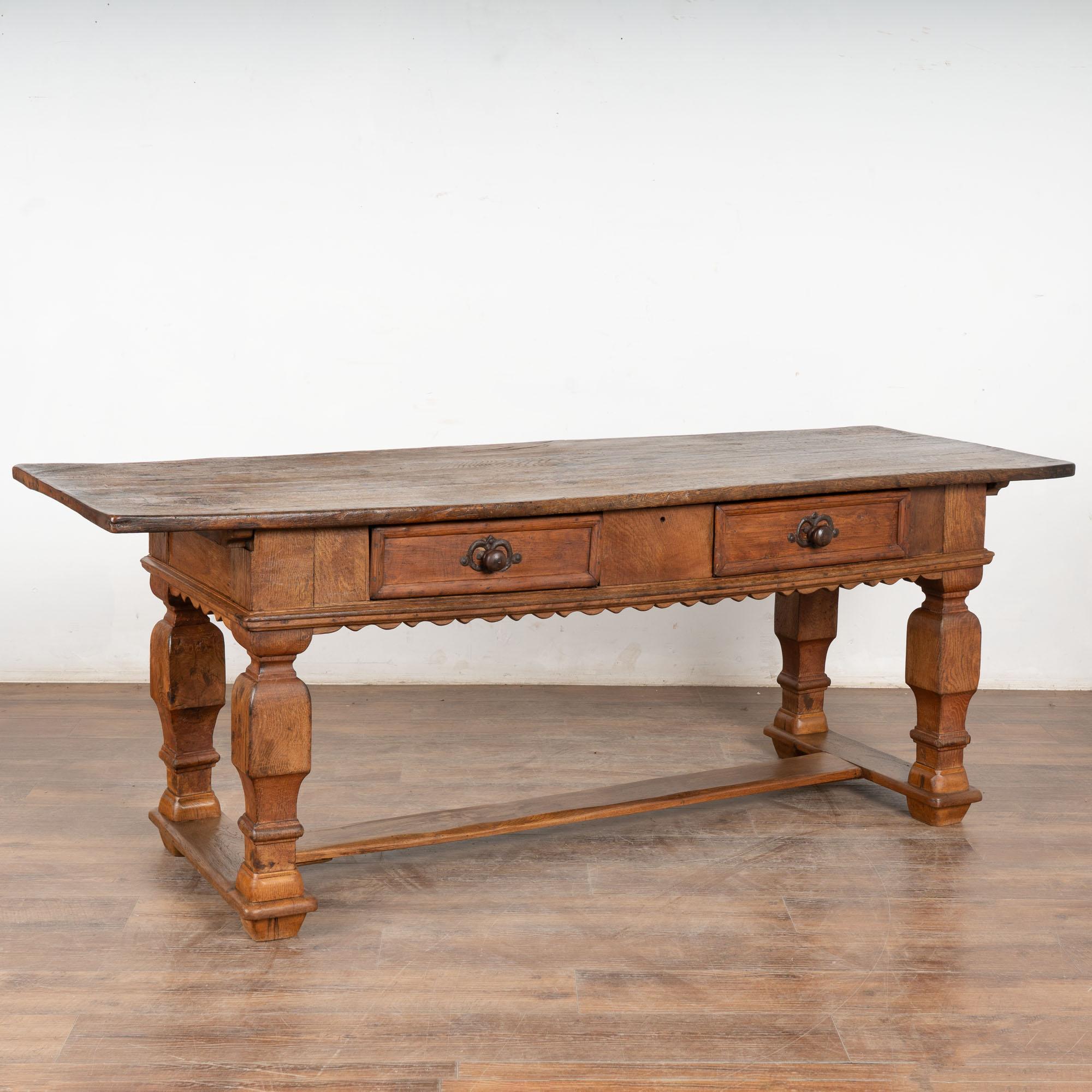 This handsome baroque style oak library or refectory table with two drawers has heavy turned legs, scalloped skirt and lower stretcher.
The top is all natural oak with nicks, cracks and stains reflecting generations of use. Note that the top has a