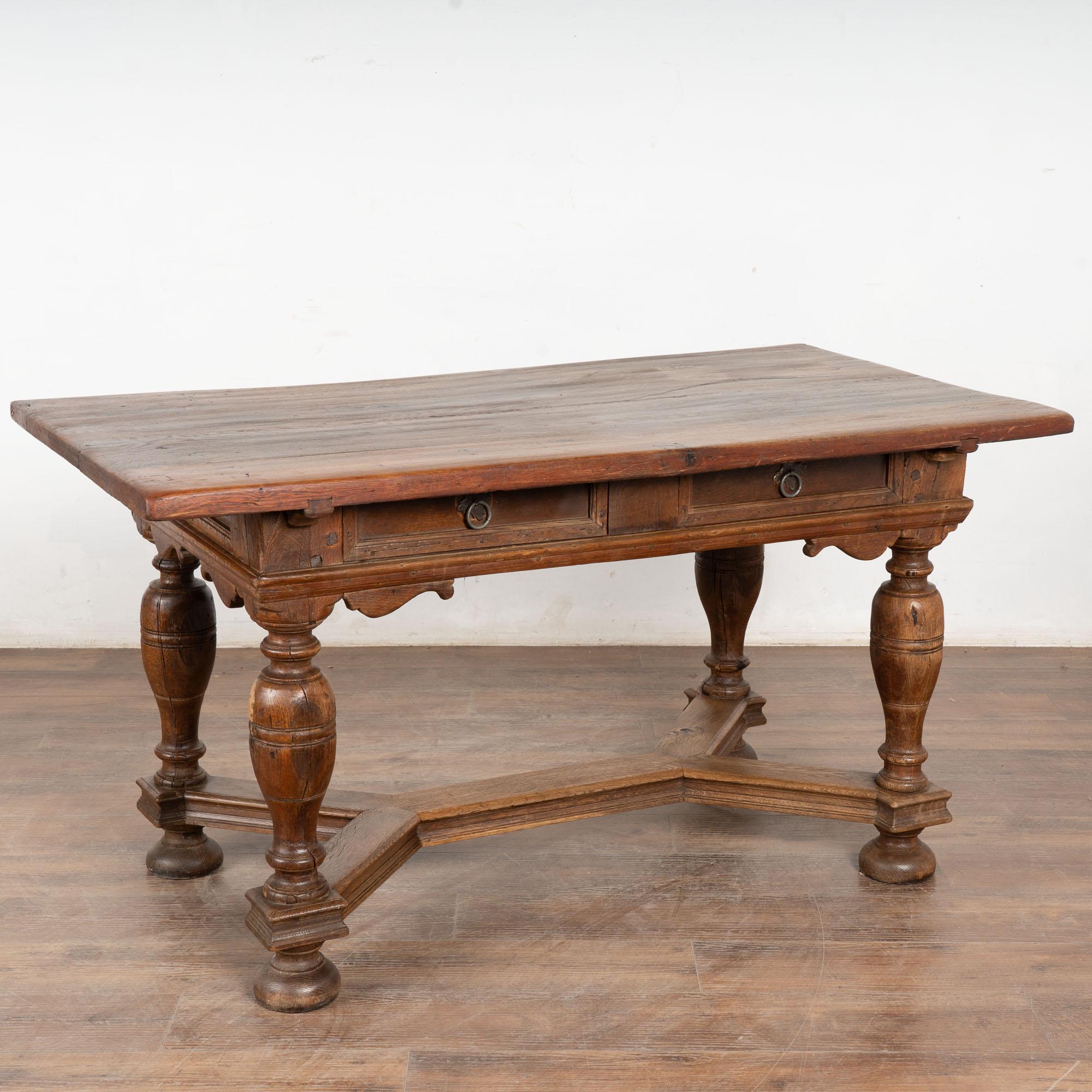 Cette belle table de bibliothèque en chêne baroque avec deux tiroirs fonctionnels a des pieds fortement tournés et un attrayant châssis inférieur en X.
Notez la riche patine du sommet et les différentes couleurs des planches de bois. Les