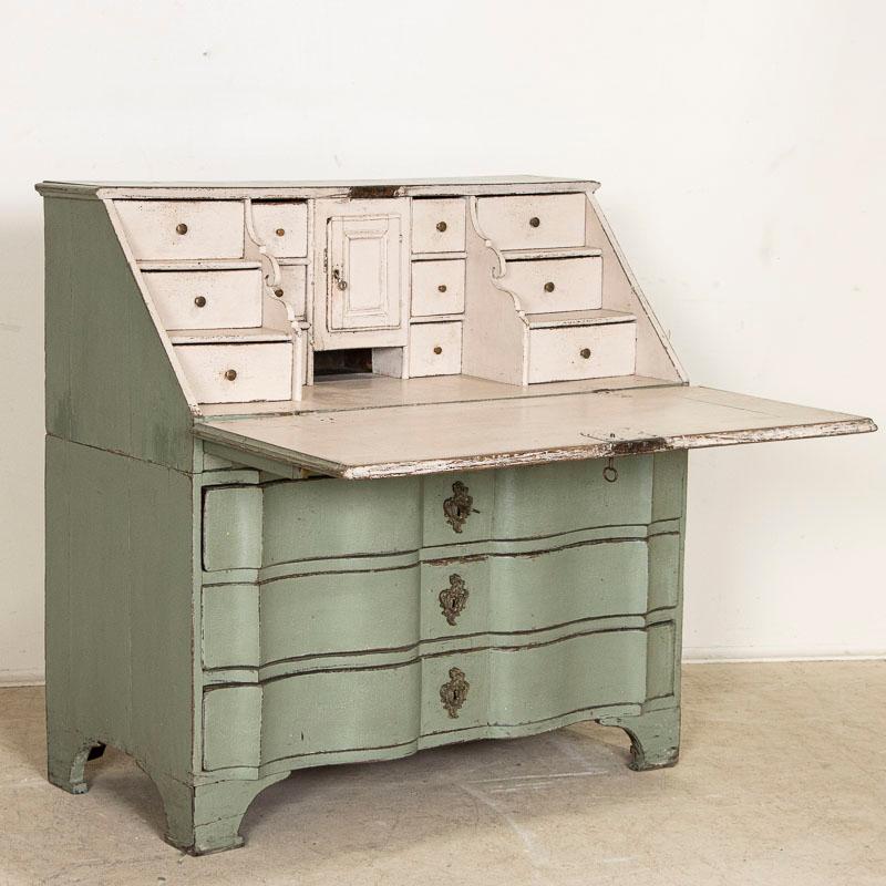 This drop front secretary is charming in every way. The soft green paint (newer, professionally applied) with undertones of blue is a lovely accent to the serpentine front drawers. The 12 petite interior drawers and central cubbie were traditional