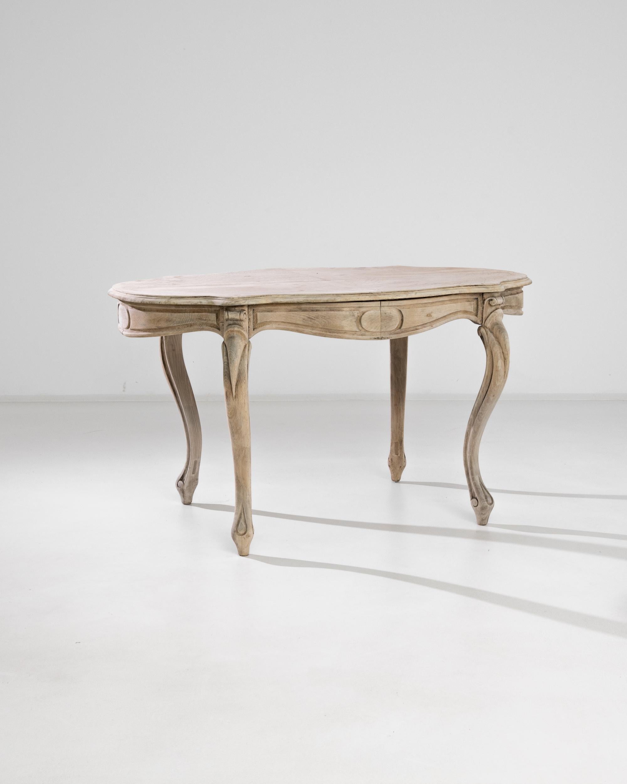 This beech table was made in France circa 1880. It adopts a peculiar shape due to the well-pronounced curvature of the cabriole legs decorated with elaborate carvings. The upper part is connected to the modestly ornamented apron with bold scrollwork