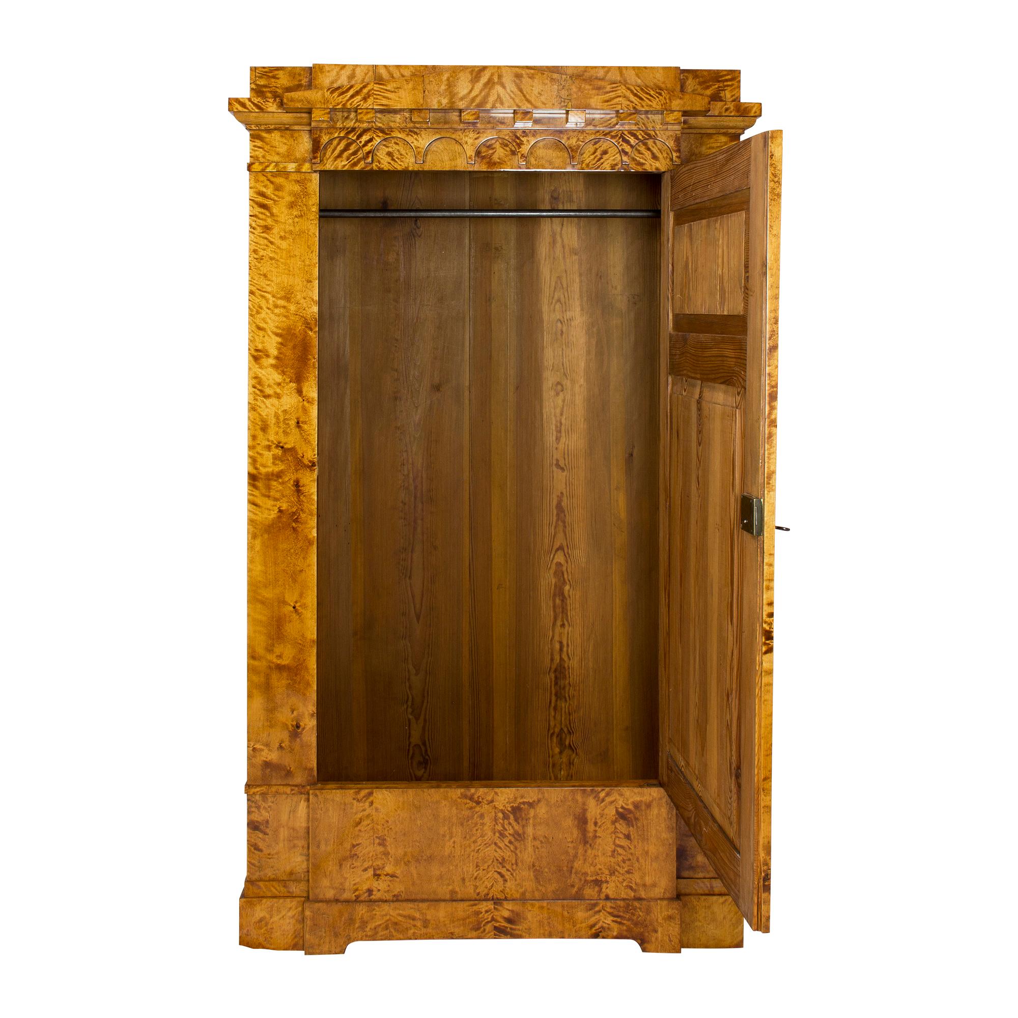 An impressive cabinet from the early Biedermeier period circa 1810, the cabinet was built with a spruce body covered with flamed birch veneer. The flamed birch, the protruding door in the centre and the shingle roof above the single-door wardrobe