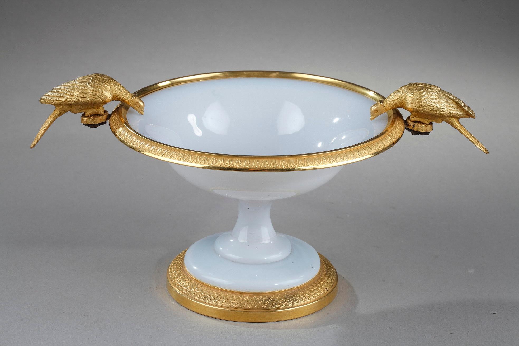 White opaline cup with gilt bronze mounts. The upper, gilded rim is finely sculpted with water-leaf.The handles are in the form of doves drinking. This motif is inspired by an antique mosaic discovered at Tivoli and mentioned by Pliny.
Dimension: