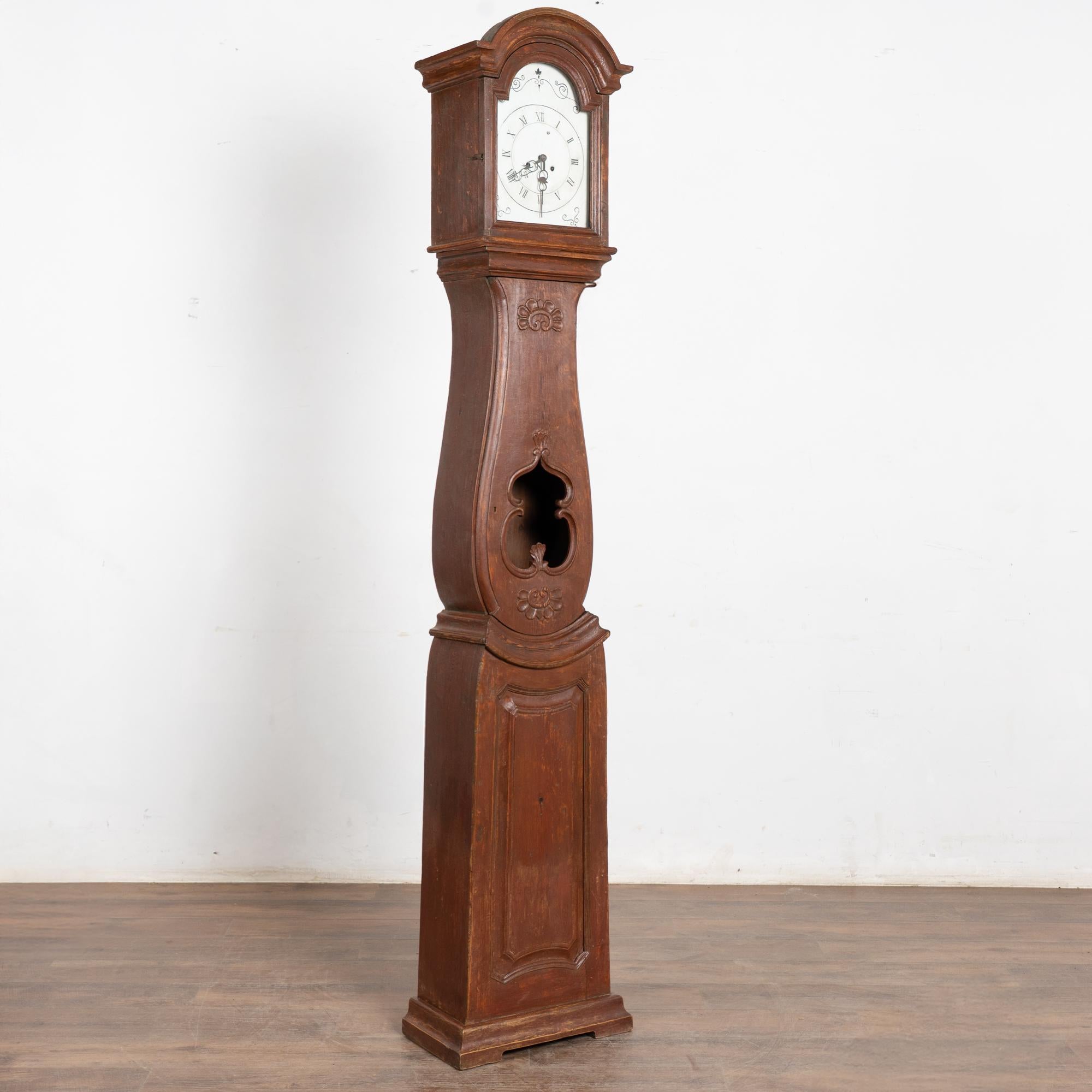 Early 19th-century Swedish Mora clock crafted in pine with an original brick-red-brown painted finish. The long case features hand-carved details, especially around the opening refered to as the 