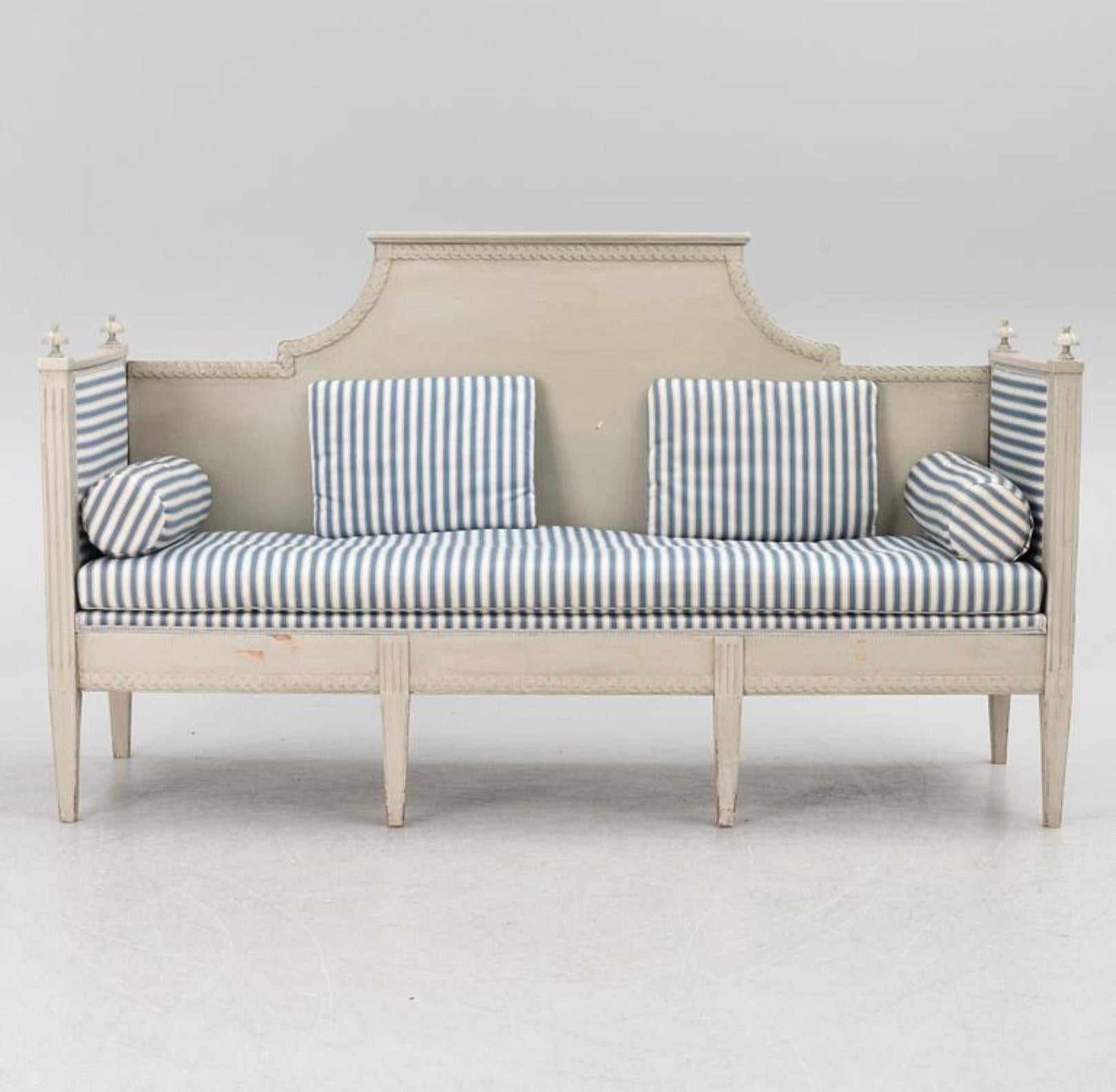 A useful and understated Swedish Gustavian sofa/bench.

Later painted in a light grey blue and upholstered in a blue stripe with cushioned sides and separate long seat cushion with bolsters,it has a typical high back and simple border decorative