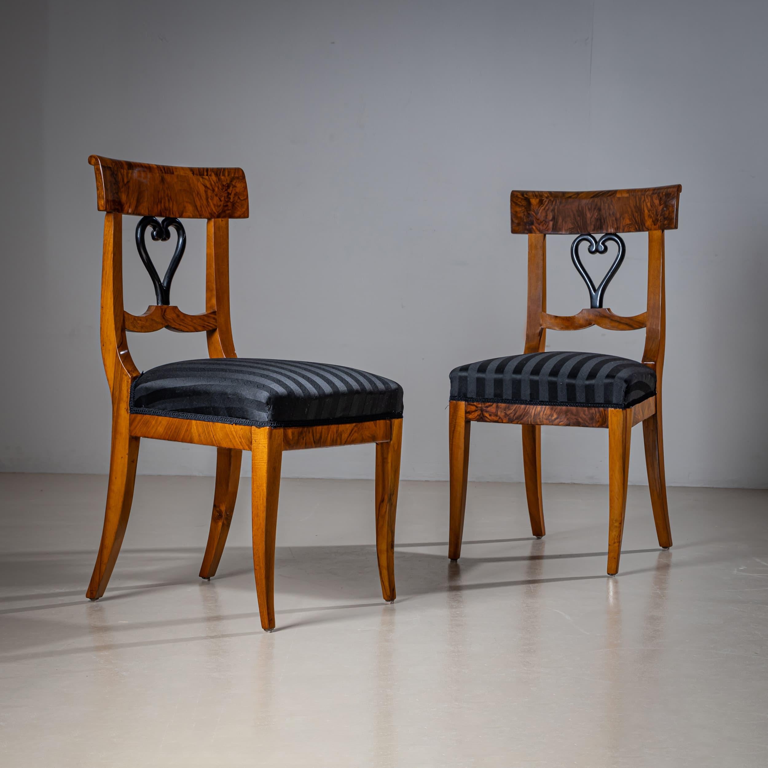 Elegantes Paar Biedermeier Beistellstühle aus Nussbaum mit herzförmiger, ebonisierter Leiste in der Rückenlehne. Die Stühle stehen auf sanft geschwungenen Säbelbeinen und sind mit einem hochwertigen, schwarz gestreiften Stoff neu gepolstert worden.