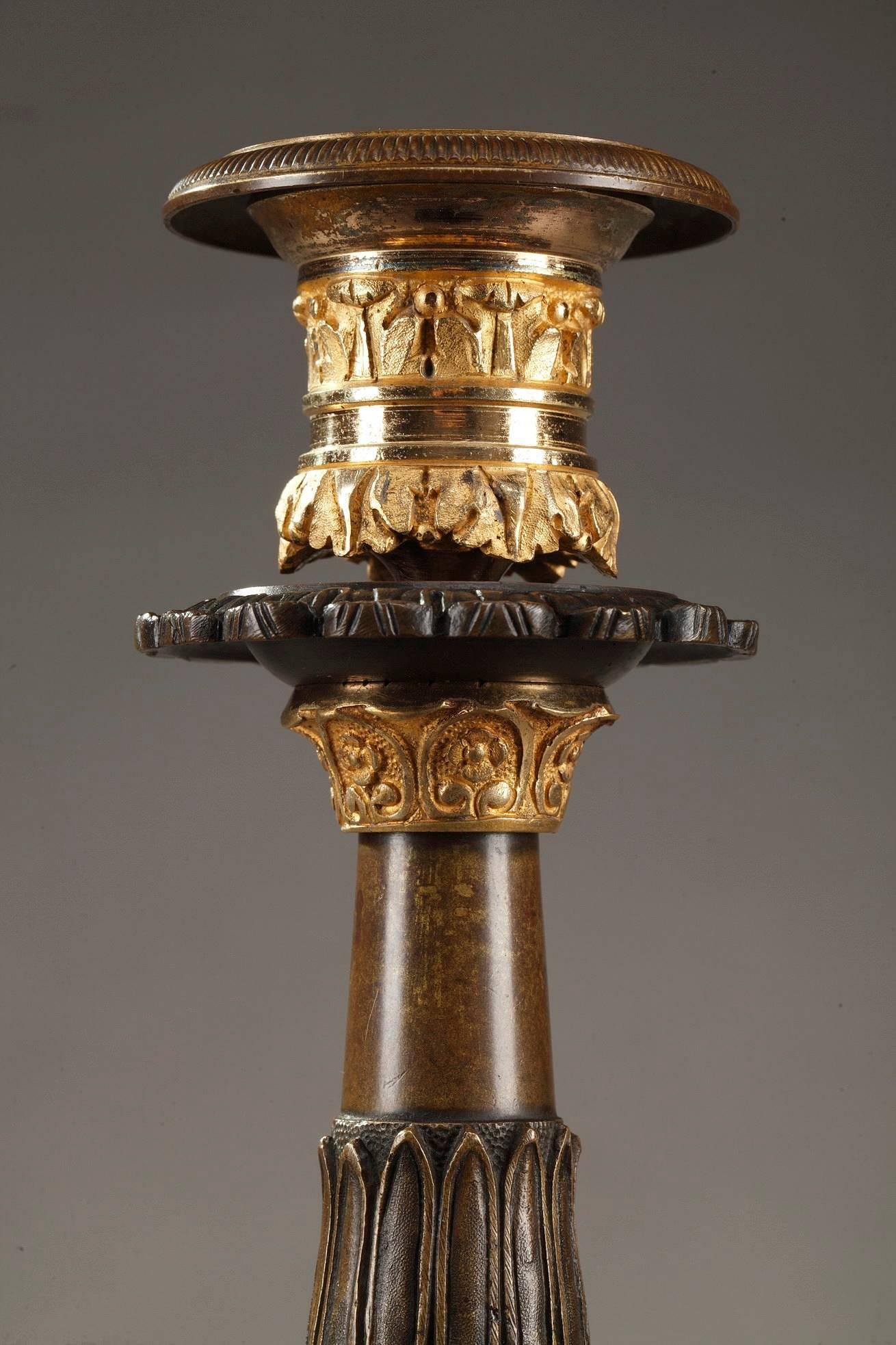 Pair of Restauration candlesticks crafted of gilt and patinated bronze resting on three foliated claw feet and a tripod base with chamfered angles. Each candlestick is richly decorated with acanthus leaf, palmettes, scrolls, water-leaf and