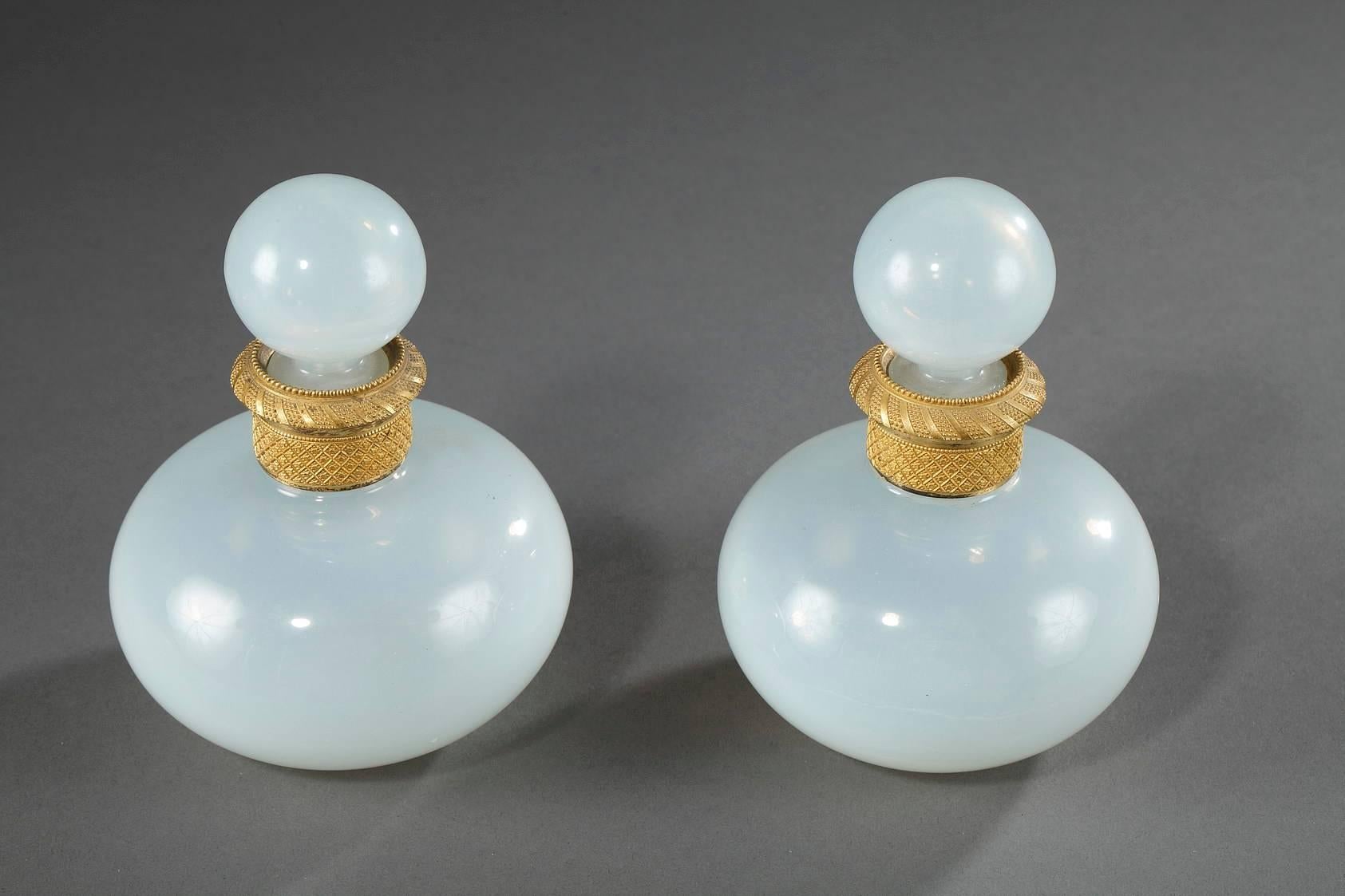 Pair of white Opaline crystal flasks with their ball-shaped stoppers. Each neck is a gilt bronze ring that is intricately sculpted with latticework, small flowers, and delicate beadwork. This exquisite example of translucent crystal is
