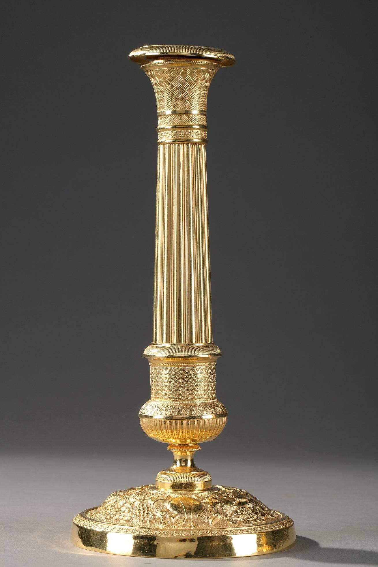 Pair of chiselled and gilt bronze restauration candlesticks, with a circular base decorated with flowers and Bacchus attributes (vine leaves, grapes and musical instruments) on a matte ground. The partially fluted stem is adorned with vine branches