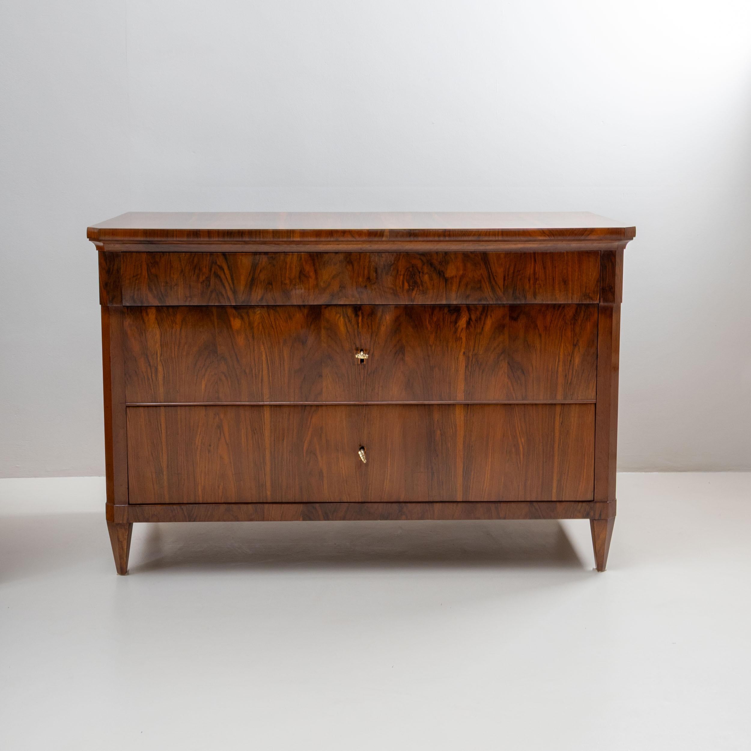Impressive pair of large Biedermeier chests of drawers, each with three drawers and chamfered corners. The top drawer projects slightly forward, accentuating the classic structure of the front. Both pieces are veneered in beautifully walnut and have