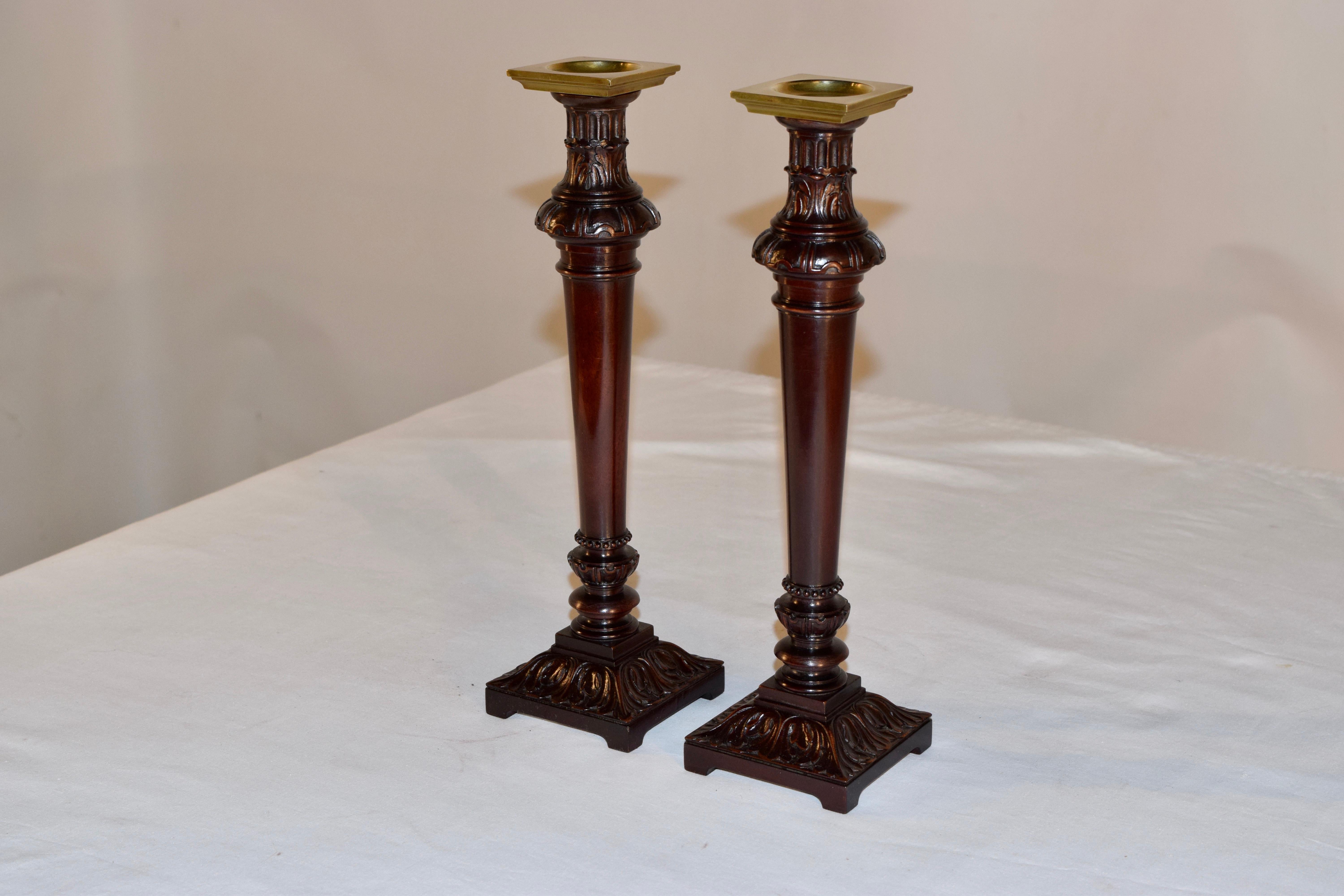 Pair of English mahogany candlesticks, circa 1810. The tops are made from heavy cast brass, and are supported on hand turned and carved decorated stems with wonderfully square pedestal bases which are also exquisitely hand carved.