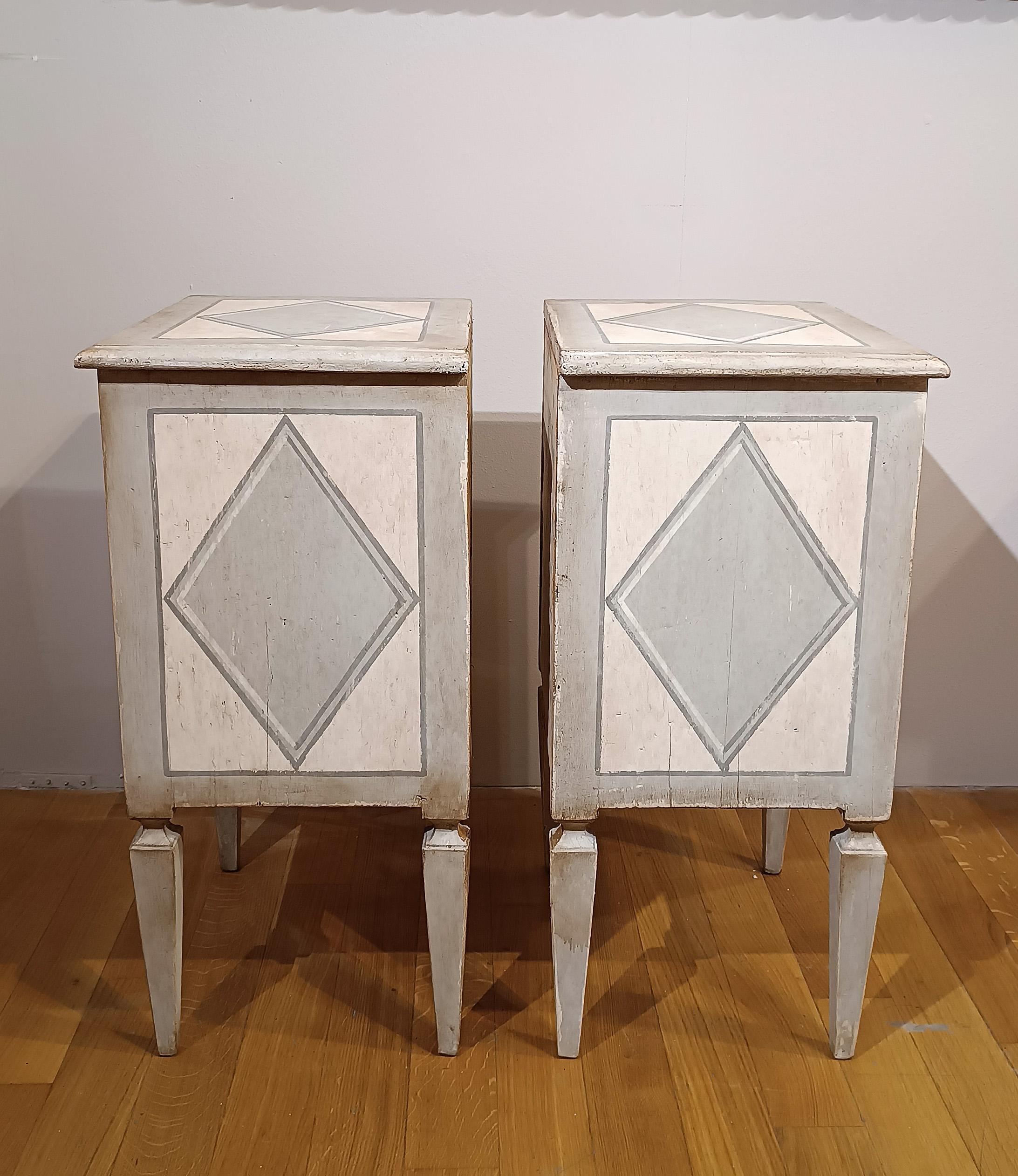 Un par de mesillas de noche neoclásicas de madera de abeto, pintadas en un esquema bicolor azul y blanco. Las superficies de todos los lados, excepto el reverso, están adornadas con refinadas decoraciones geométricas que acentúan la elegancia de la