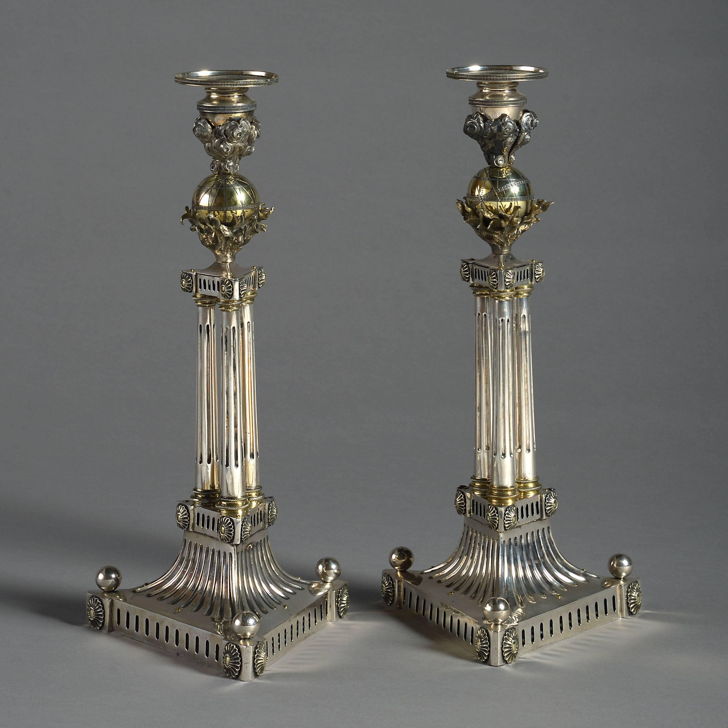 A rare and unusual pair of architectural candlesticks, each with a the socle set upon cut steel smoke clouds an etched globe and cut steel flames above fluted cluster columns, all set on triangular bases with fluted sides ball finials and paterae.