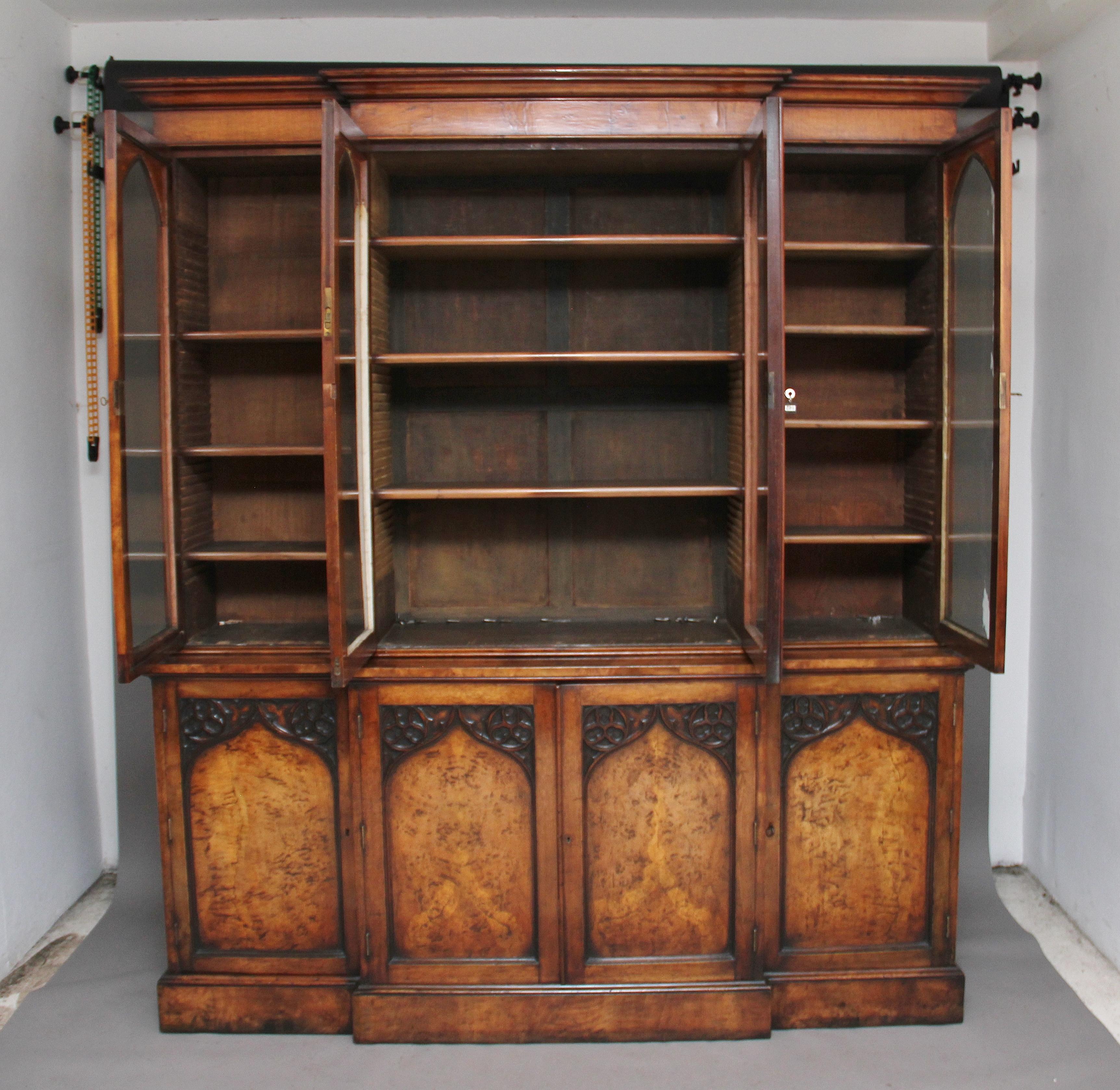 A fabulous early 19th century pollard oak and walnut breakfront bookcase in the Gothic revival style, the stepped moulded cornice above four large glazed doors with Gothic arched frames with carved leaf decoration in the corners, the doors opening