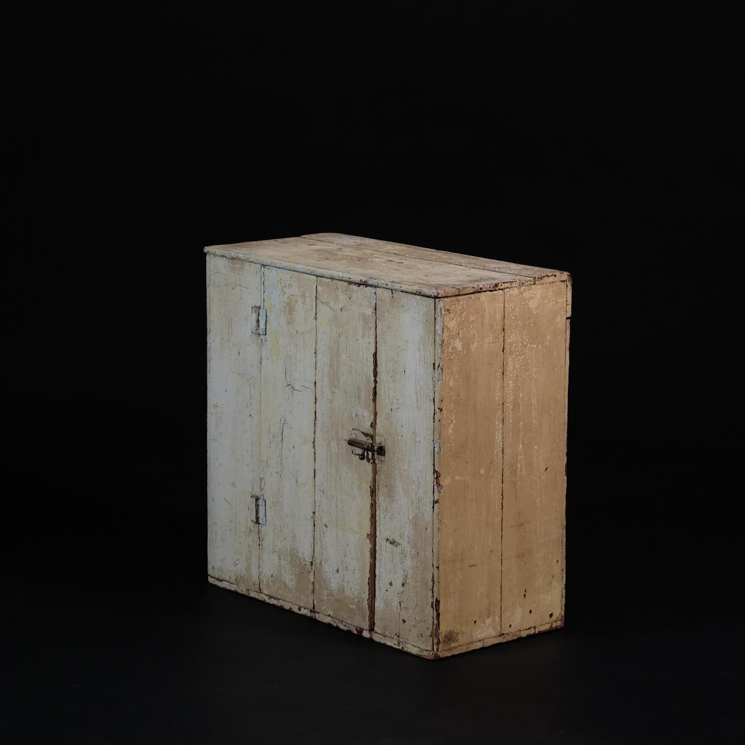 A small pine boarded cupboard in layers of old crusty paint. Door opening in centre with a nice brass bolt fastner, revealing a single shelved interior. Very evocative and perfect for the rustic farmhouse style kitchen. Likely West Country in
