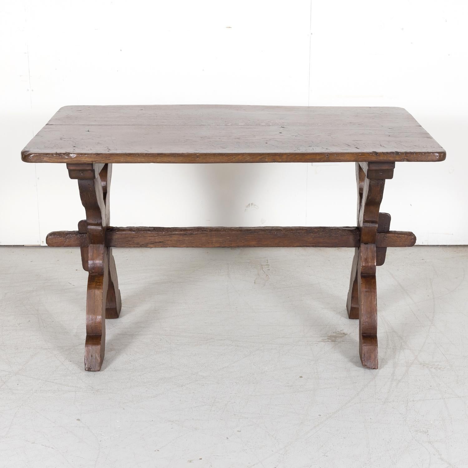 A rustic early 19th century primitive side table handcrafted of solid oak near Tarragona in the Catalan region, circa 1810s, having a rectangular plank top raised on a scalloped X base with a wood stretcher. The beautifully aged patina adds instant