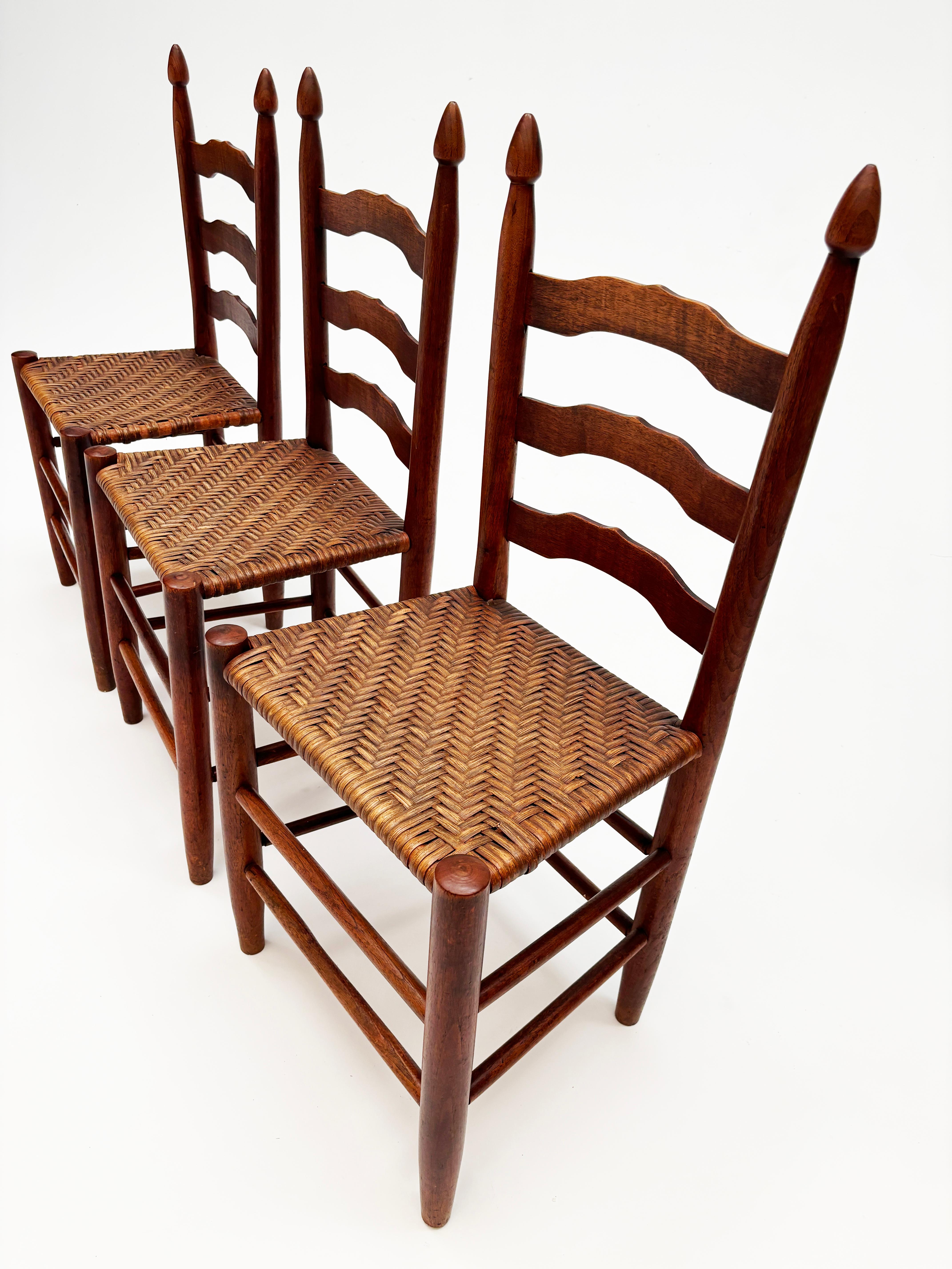 Ces chaises à dossier en échelle à 3 places constituent un ensemble magnifique et mystérieusement unique. Fabriquées en bois dur, chacune de ces chaises a été sculptée à la main avec des sièges en canne à chevrons tissés à la main. D'une couleur