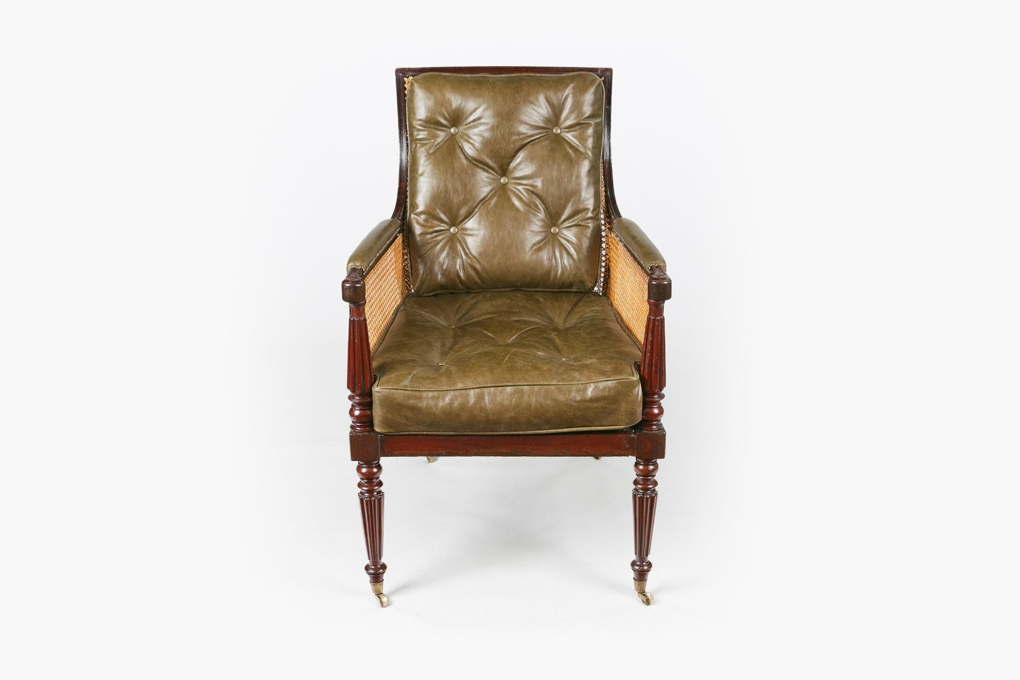 Early 19th century Regency bergère library chair, the rectangular and shaped moulded mahogany frame hand caned with downswept moulded arms with green studded green leather raised over turned and fluted supports with loose green leather buttoned
