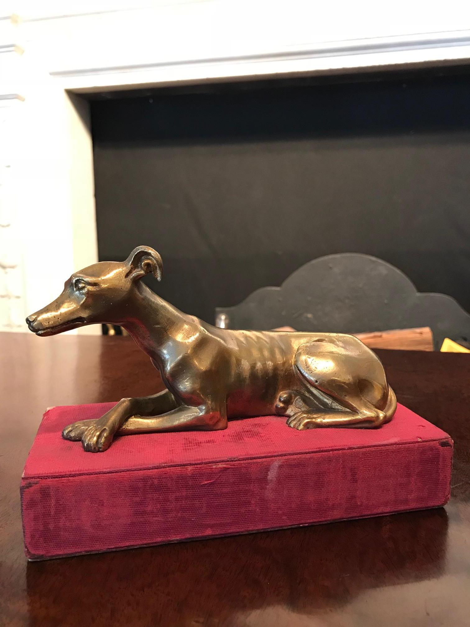 Early 19th century Regency brass paperweight in the form of a recumbent greyhound raised over cloth covered base.