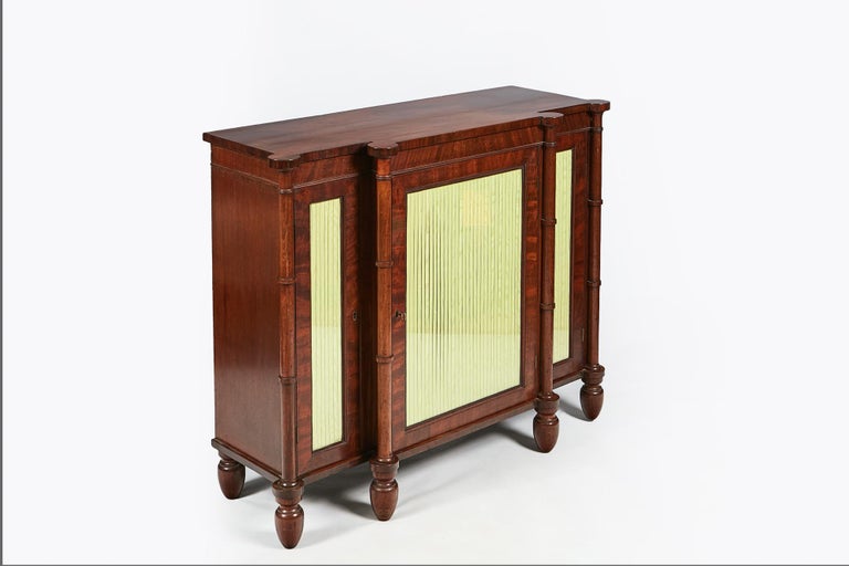 Early 19th century Regency breakfront flame mahogany cabinet, the moulded top over three glass doors flanked with moulded columns terminating on toupie foot, circa 1810.