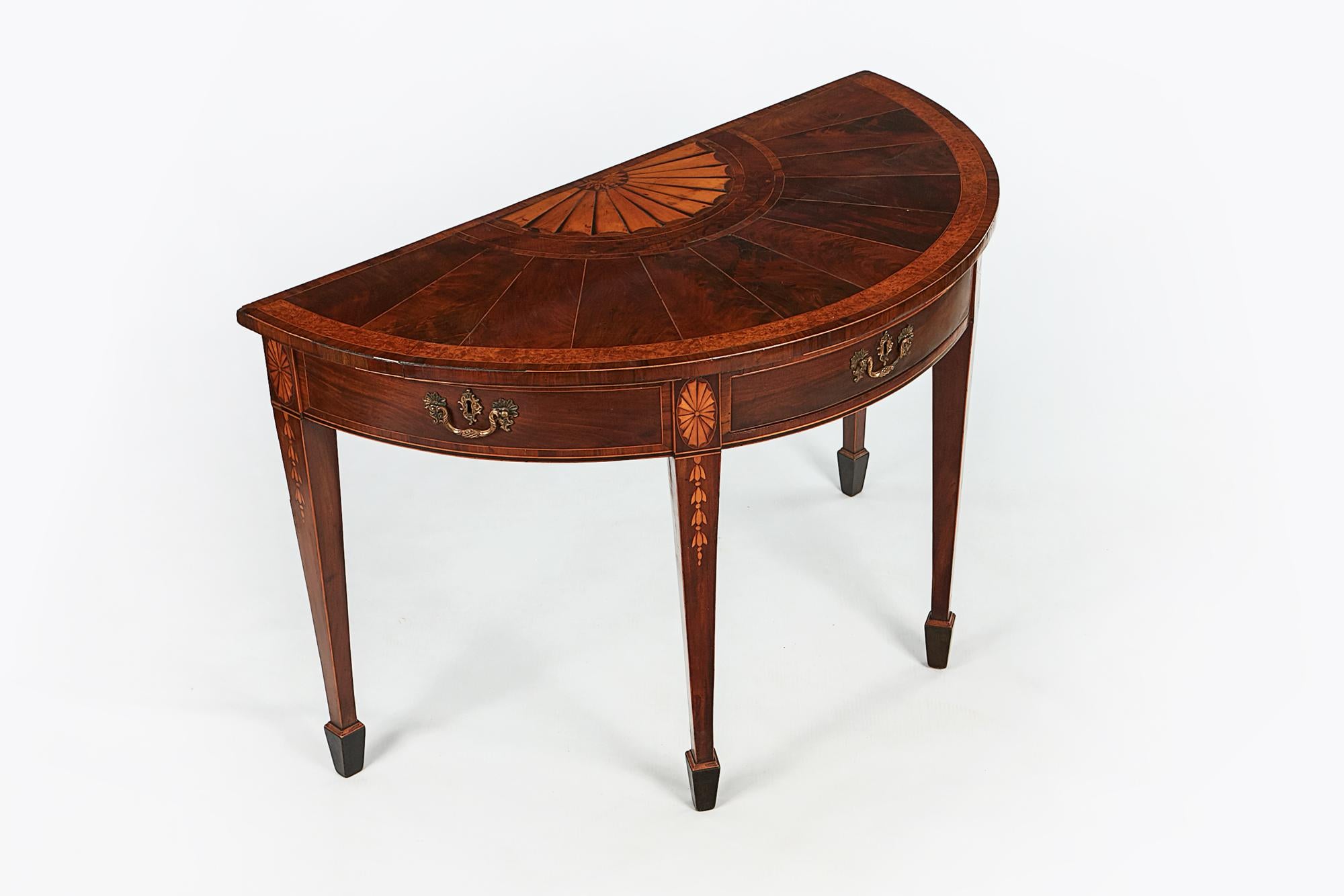 Early 19th century Regency demilune table in the style of William Moore, the fan inlaid top above banded frieze with three cross beaded drawers with brass pulls and escutcheons raised over tapering square legs with floral inlay terminating on spade