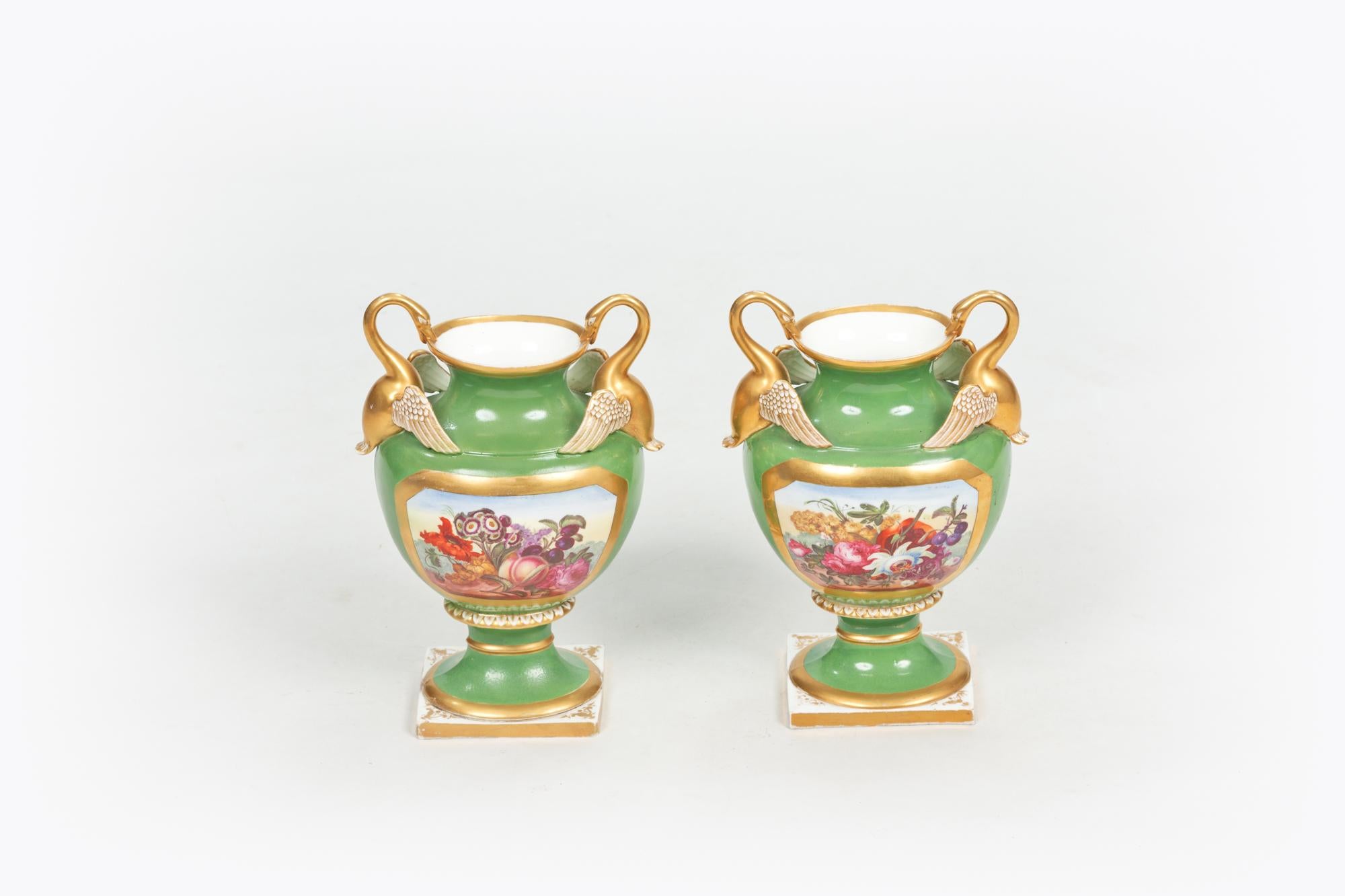 Frühes 19. Jahrhundert Regency-Derby-Vasenpaar, der umgedrehte Rand mit vergoldetem Band auf weißem Grund erhebt sich über einem Balusterkörper mit grünem Grund und vergoldeter Kartusche, die ein polychromes Blattmotiv zeigt, flankiert von zwei