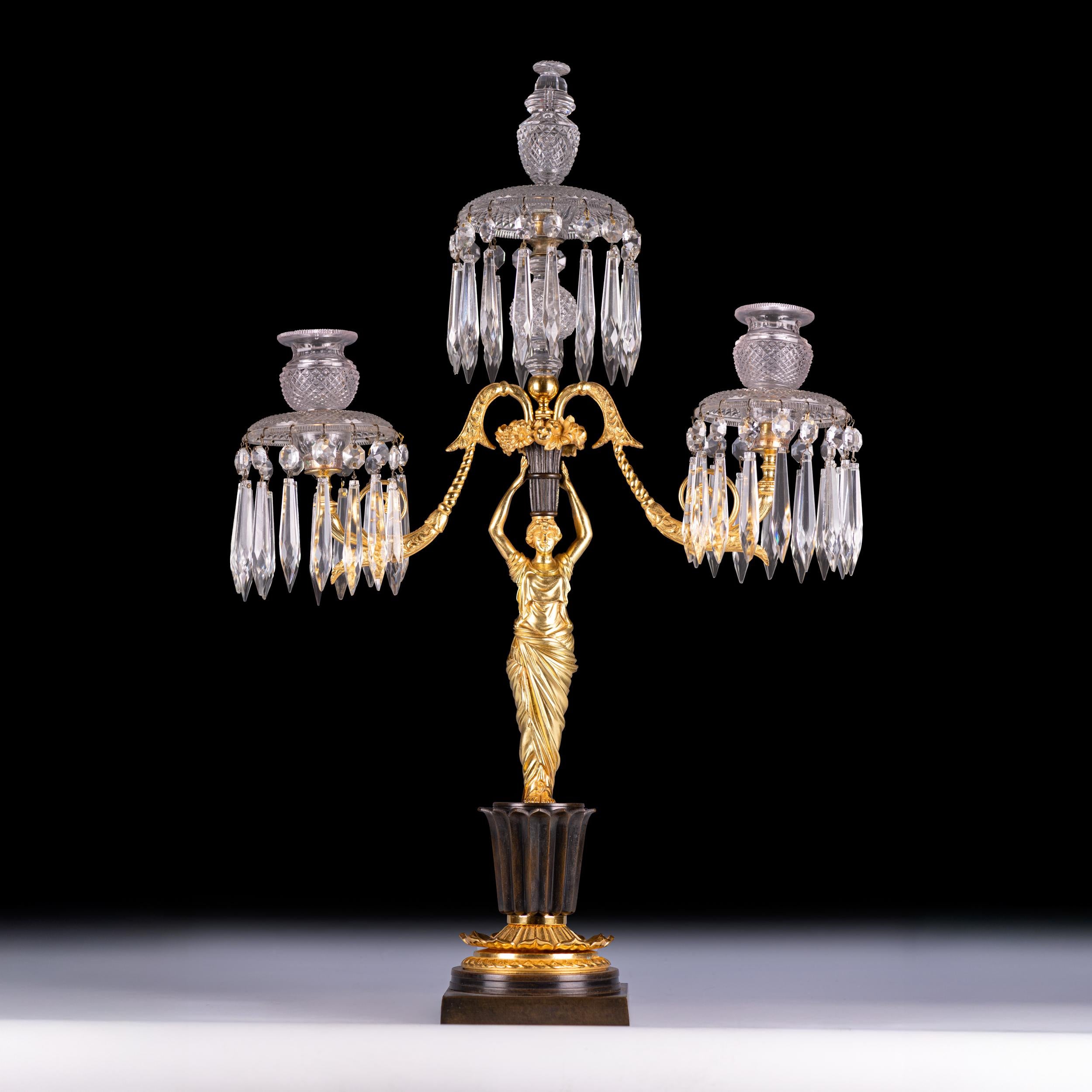 An exquisite Regency period three-light candelabrum, featuring a finely cast and chased gilt-bronze female figure in classical drapery, standing on a patinated and gilt-bronze socle base. She supports an urn issuing three scrolling arms adorned with