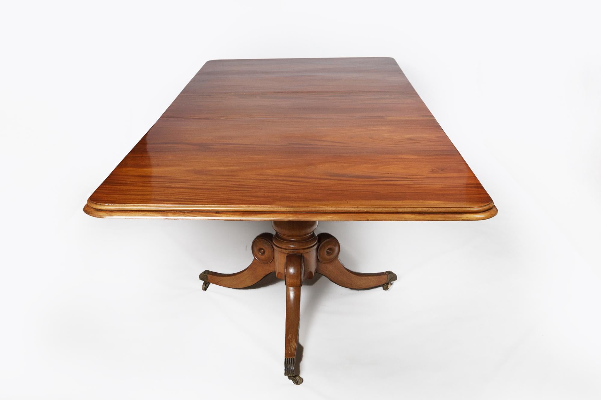 Early 19th Century Regency mahogany extendable dining table raised on two trefoil lotus pods supported by outswept legs. Terminating on reeded brass toe caps and casters.