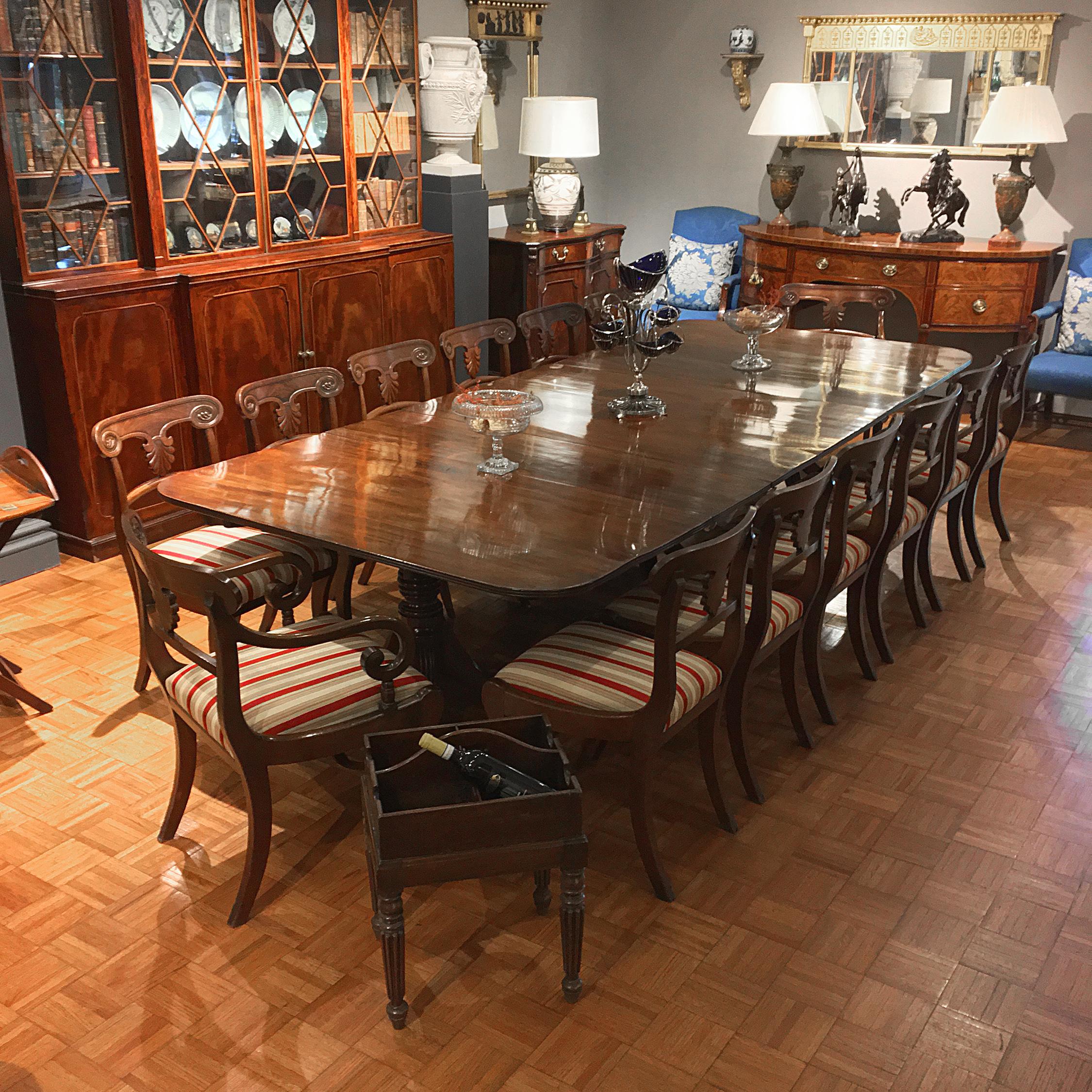 This early 19th century English Regency dining table, of a rich and lovely grained mahogany, has a reeded edge and two center leaves, and is supported by three turned pedestal bases, each with four reeded and splayed legs, with brass caps and