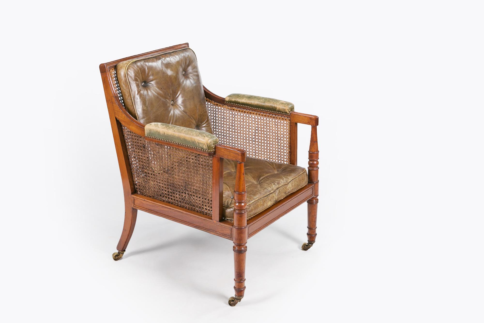 Early 19th century Regency matched pair of mahogany bergere library chairs, the rectangular moulded frame, caned with downswept arms, one chair with moulded arms with studded green leather, the other reeded, both with turned supports, the loose