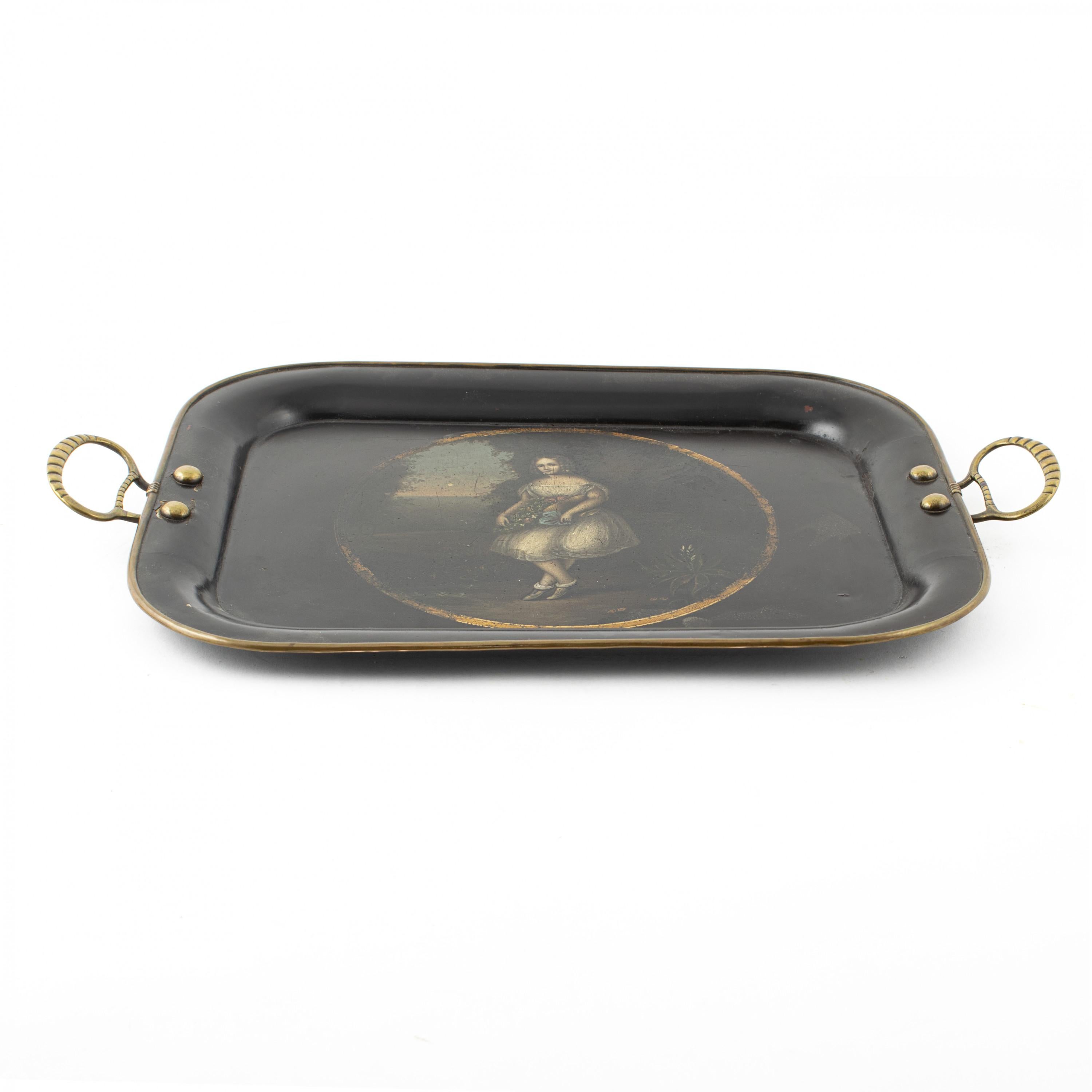 A small rectangular Regency toleware tray, with brass loop handles on the side.
The center of the tray is decorated with a hand painted portrait of young woman, with a basket of flowers, standing in a landscape scene.
   