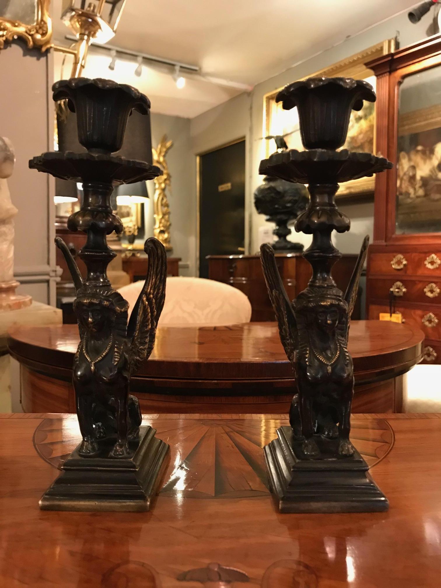 Early 19th century Regency pair of bronze candlesticks in the form of winged sphinx raised over stepped plinth surmounted with ornate candle nozzle with foliate motif.