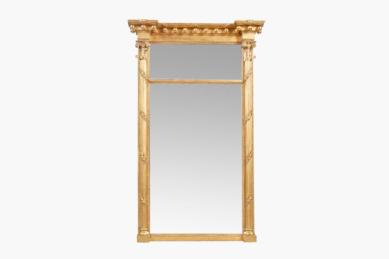 Early 19th century Regency pair of compartmental mirrors, the overhanging broken pediment stepped cornice with reeding, ribbon twist and ball decoration raised above two bevelled mirror plates set within giltwood frame of banded foliate motif