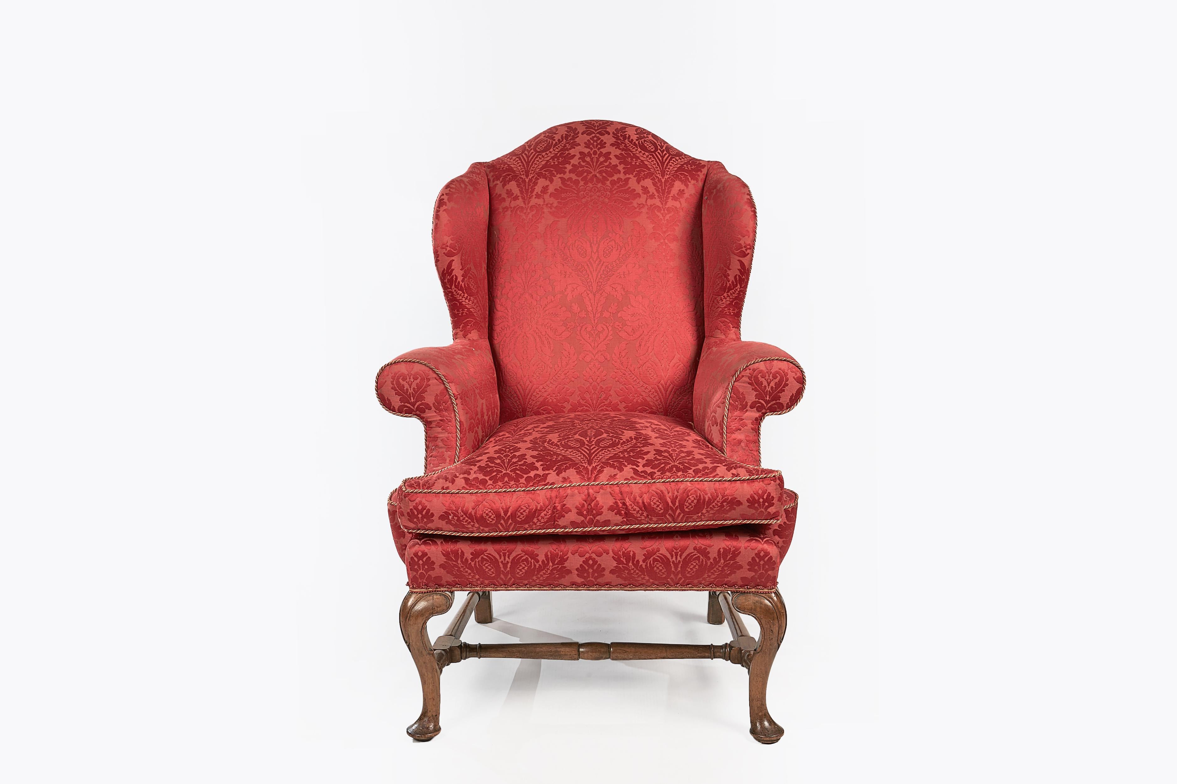 Early 19th century Regency pair of walnut wing chairs, the shaped back with outscrolled wings and arms raised over moulded cabriole leg joined with turned H stretcher terminating on pad foot.